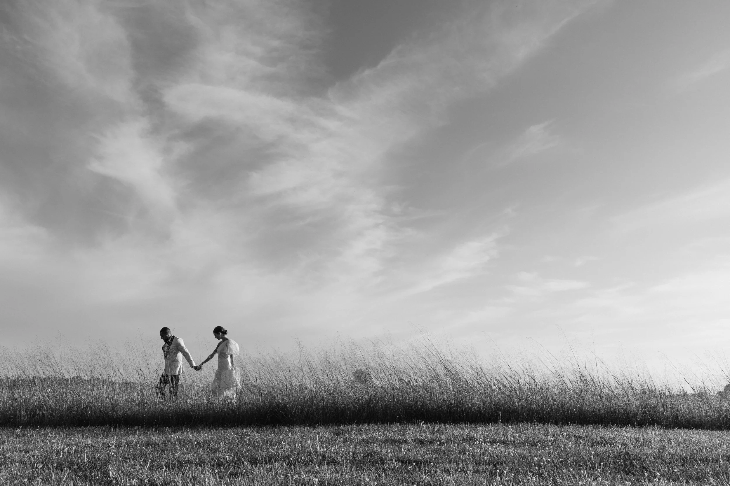 bride and groom walking through a field