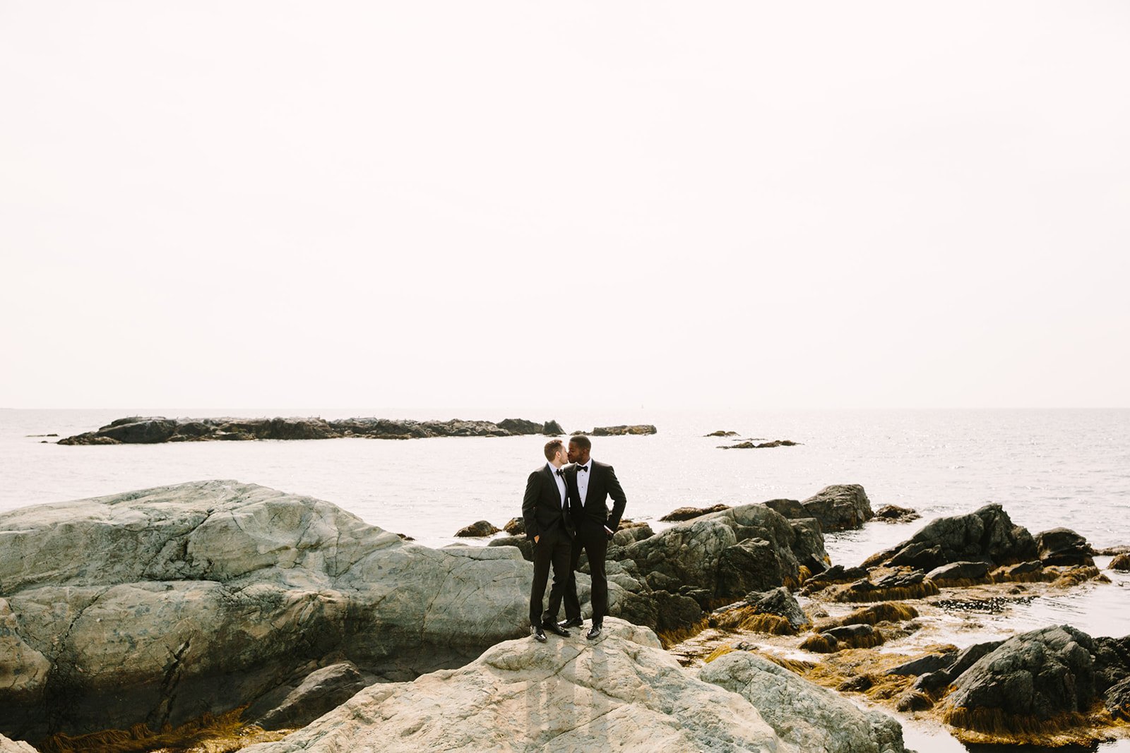 two grooms kissing on a rocky coast