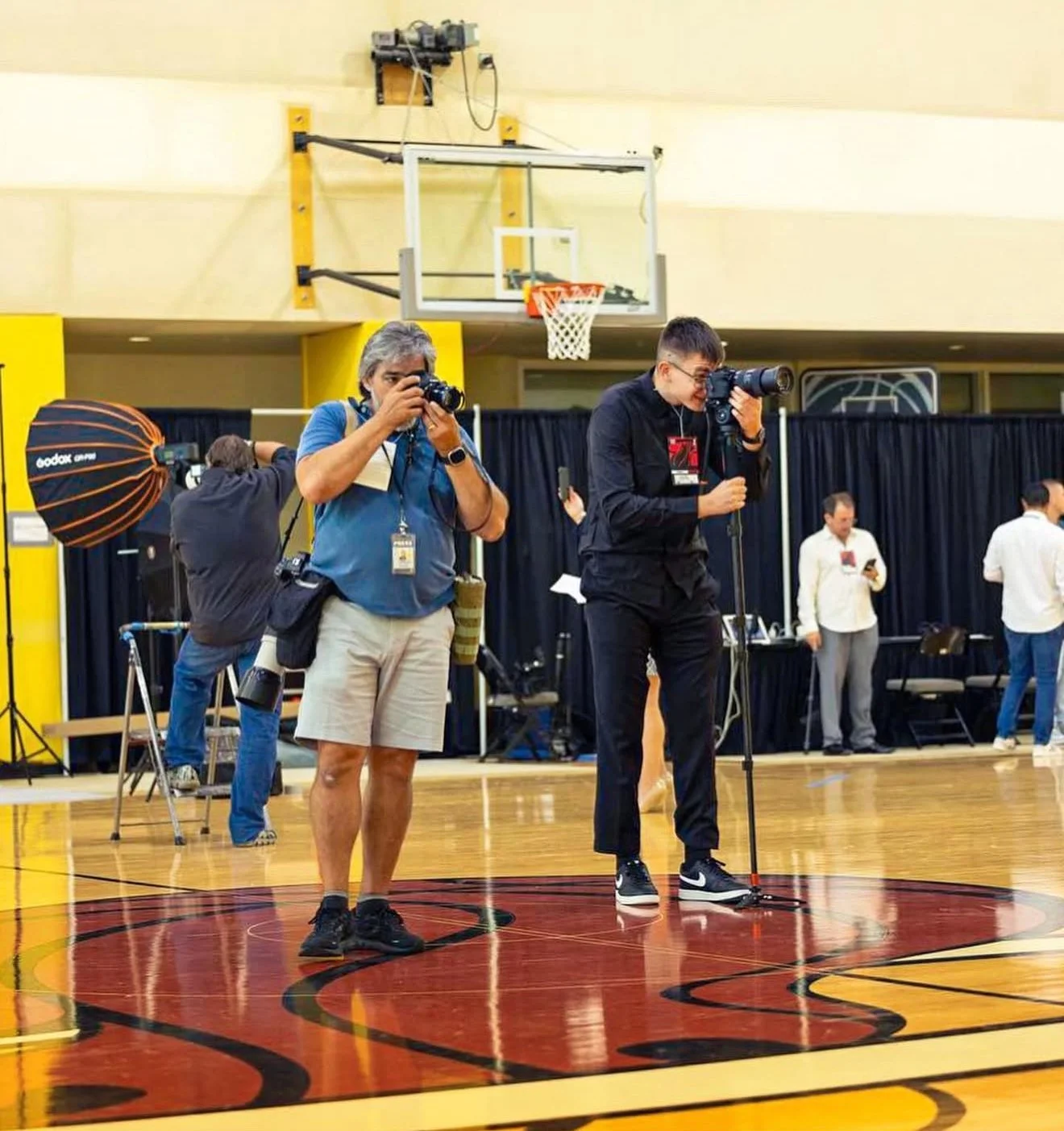 Photographers taking pictures at an indoor basketball court during an event.