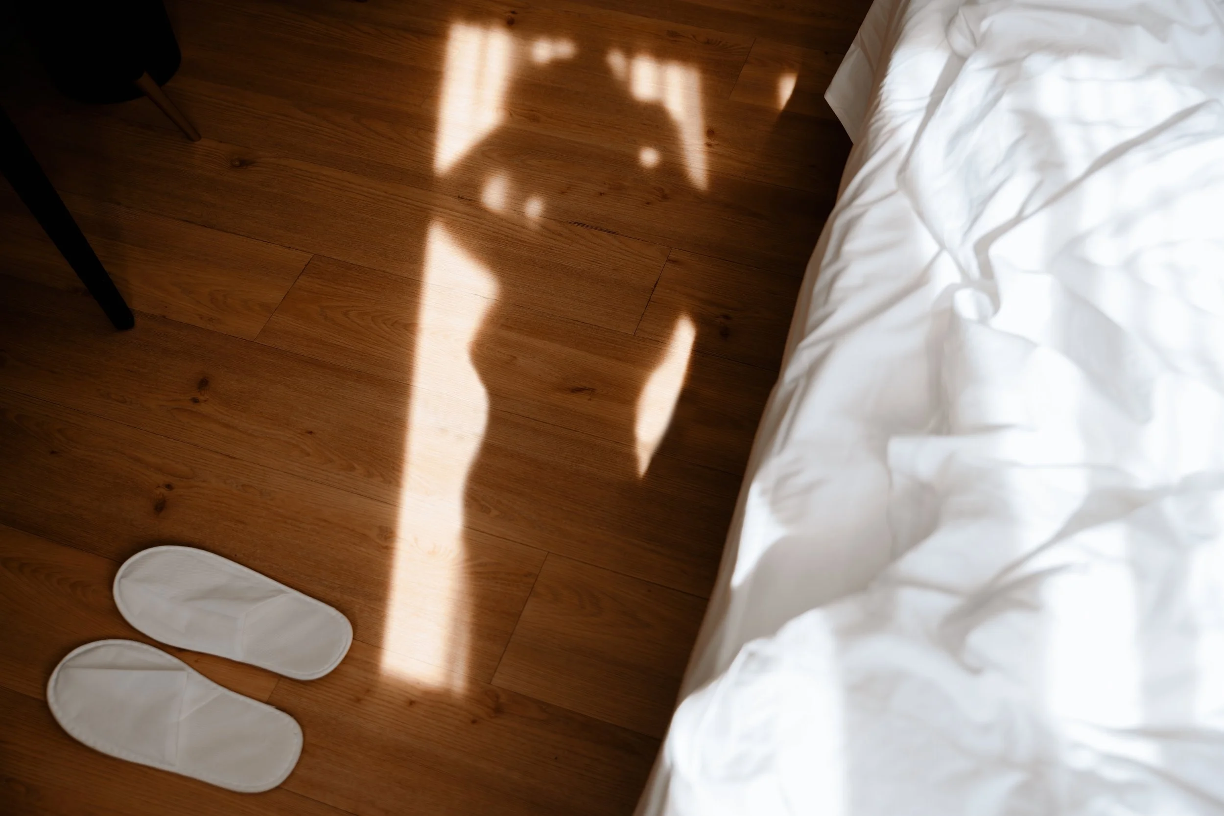 image of the shadow of a woman standing by a bed with slippers on the flooor