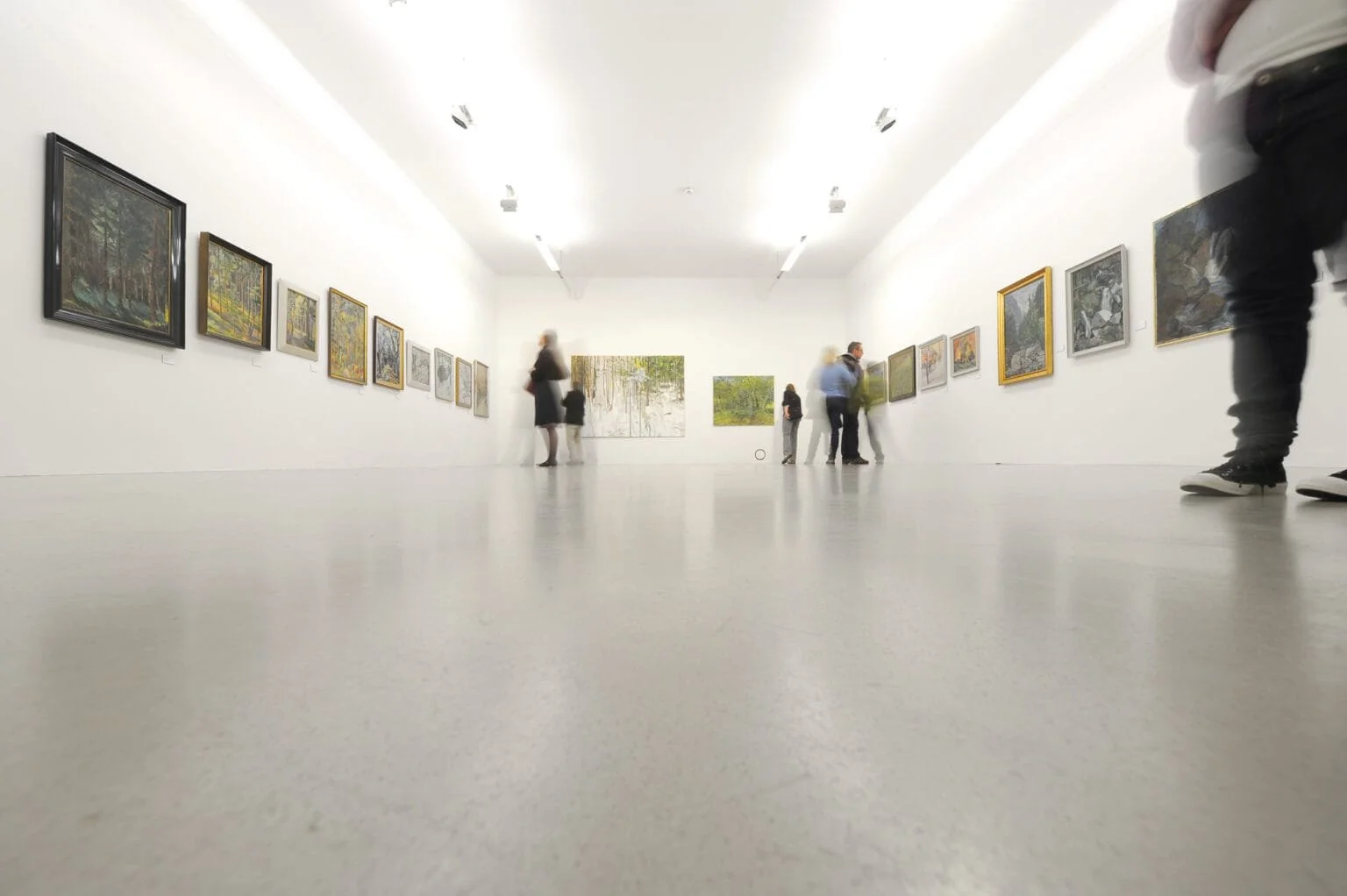People viewing artwork in an art gallery with white walls and a minimalist design.
