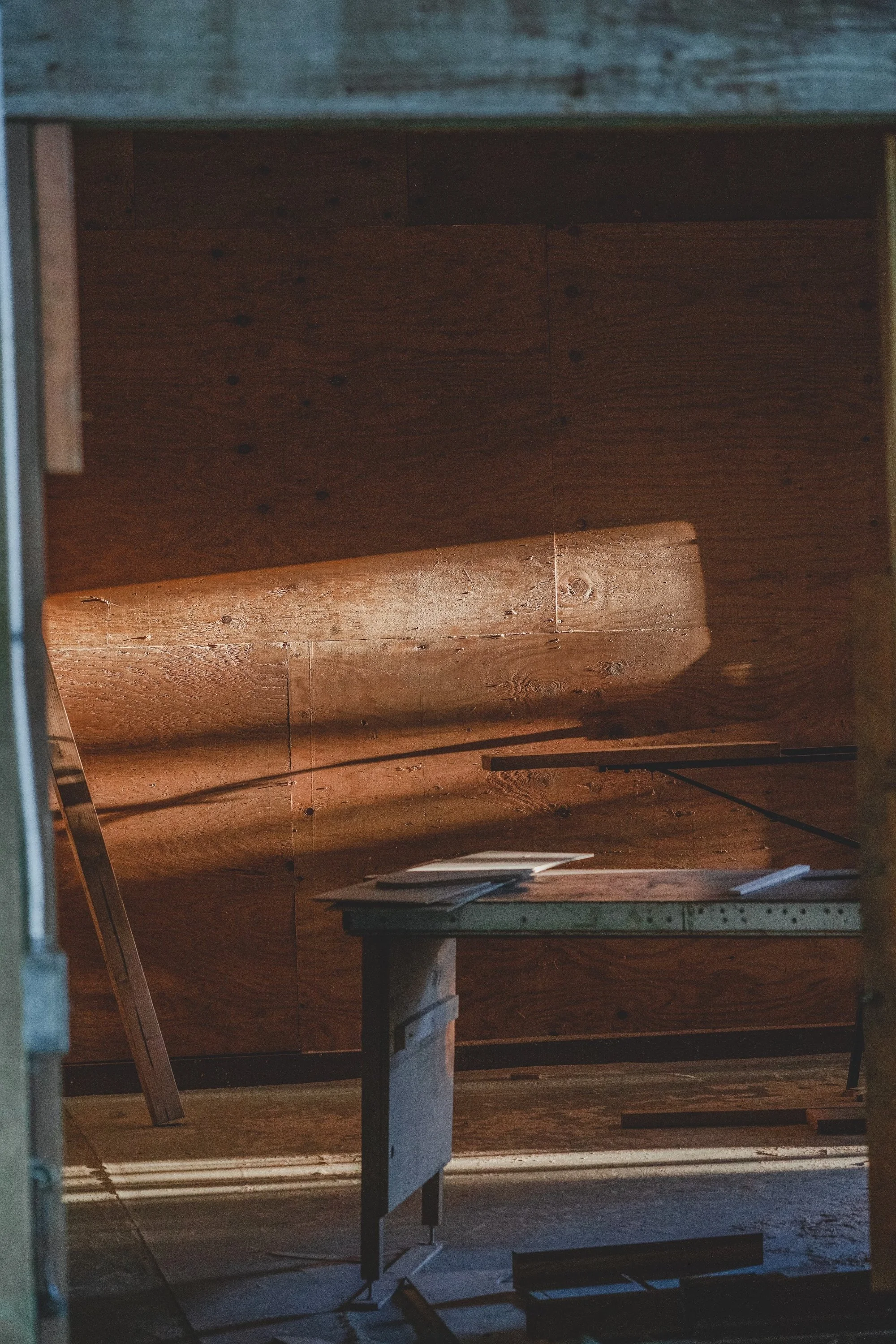 Interior of an art workshop with a wooden workbench and wood panels on the walls, sunlight casting shadows.