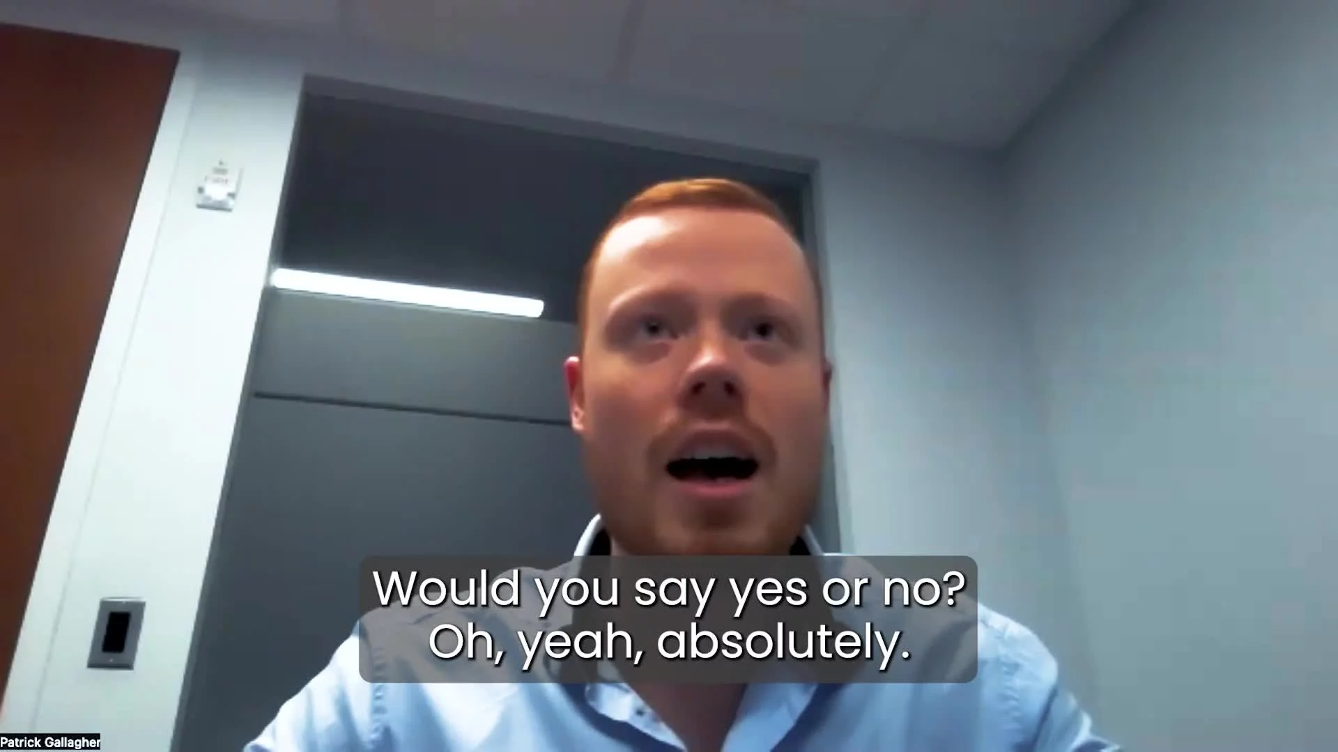 A man with red hair wearing a light blue shirt appears to be speaking in an office, with subtitles reading "Would you say yes or no? Oh, yeah, absolutely."