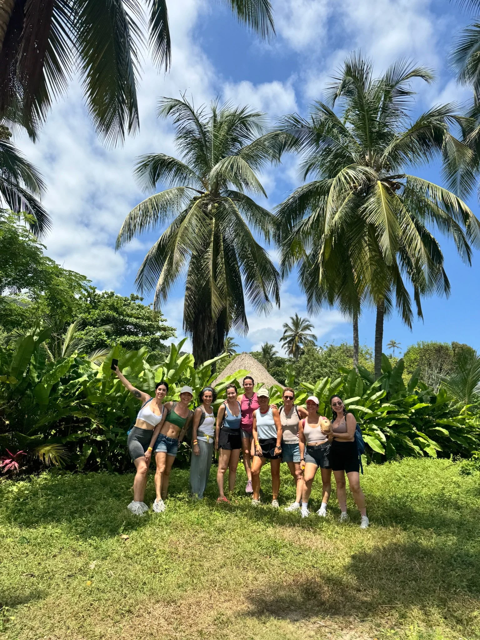 Grupo de personas sonrientes en un entorno tropical con palmeras y cielo azul.