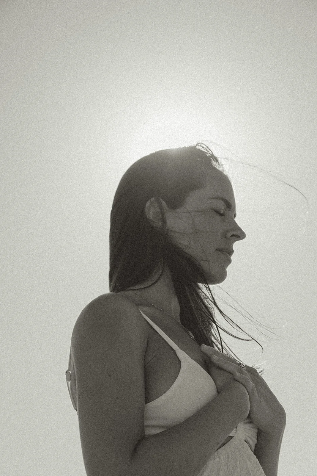 Mujer con cabello mojado, perfil, con los ojos cerrados, tocándose el pecho, en tonos sepia.
