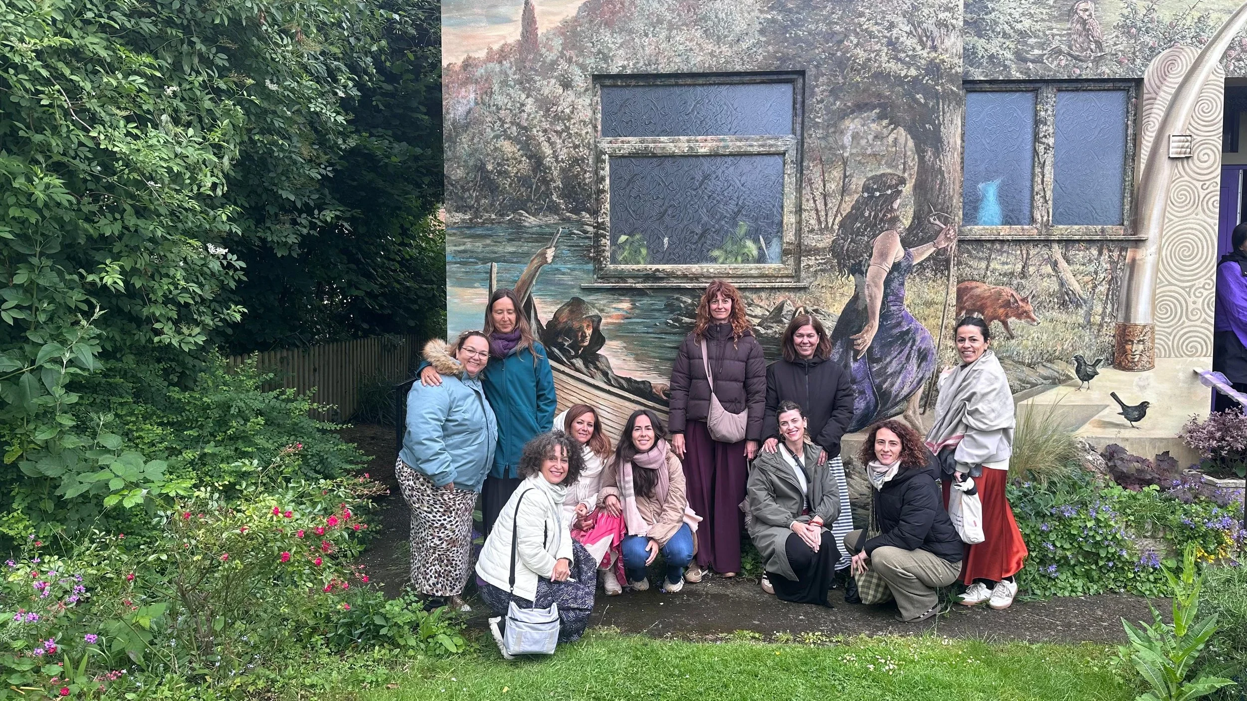 Grupo de personas posando frente a un mural naturalista con escenas de la naturaleza, rodeados de plantas y flores.