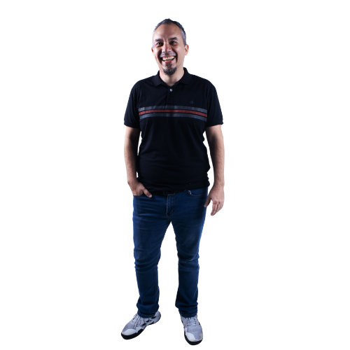 Smiling man standing with hands in pockets, wearing a black polo shirt with red and white stripes and blue jeans.