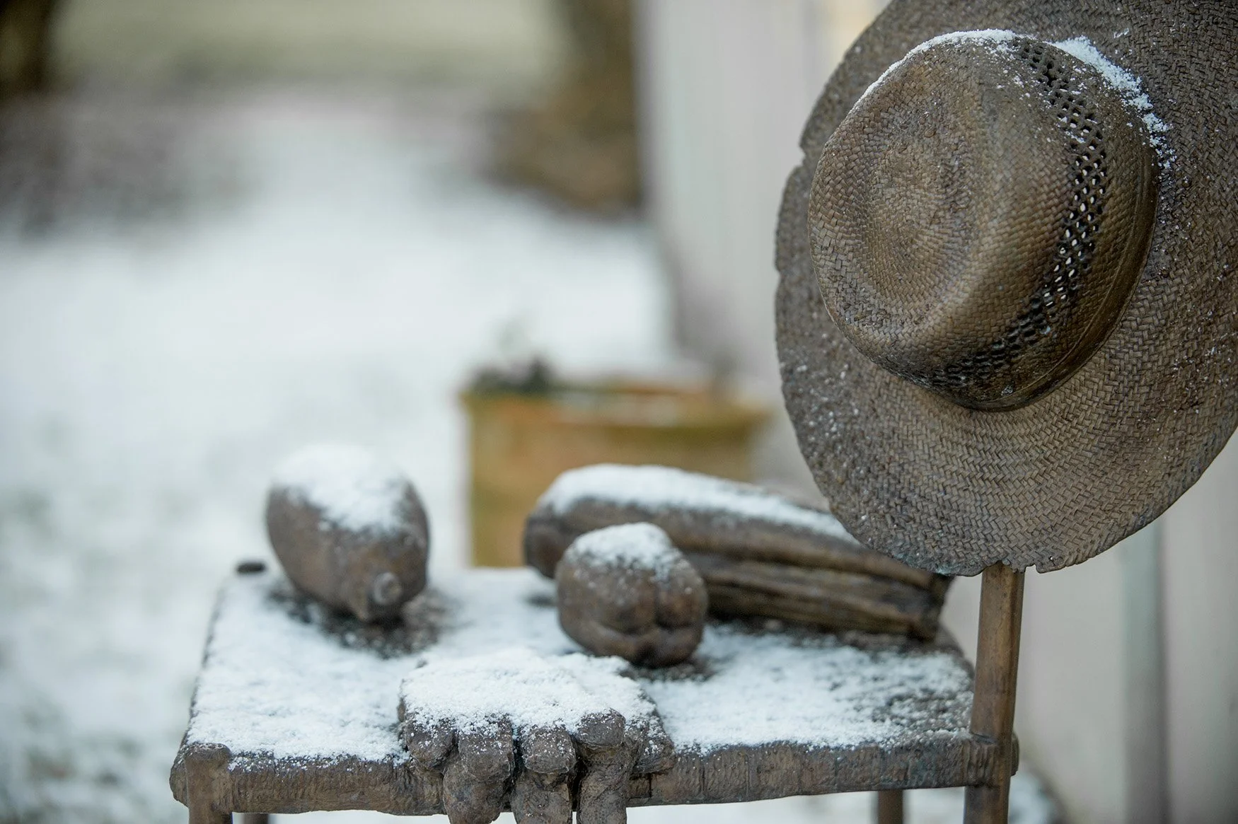Bronze sculpture garden chair vegetables and gardening gloves on seat straw hat hanging on chair back snow settling on chair