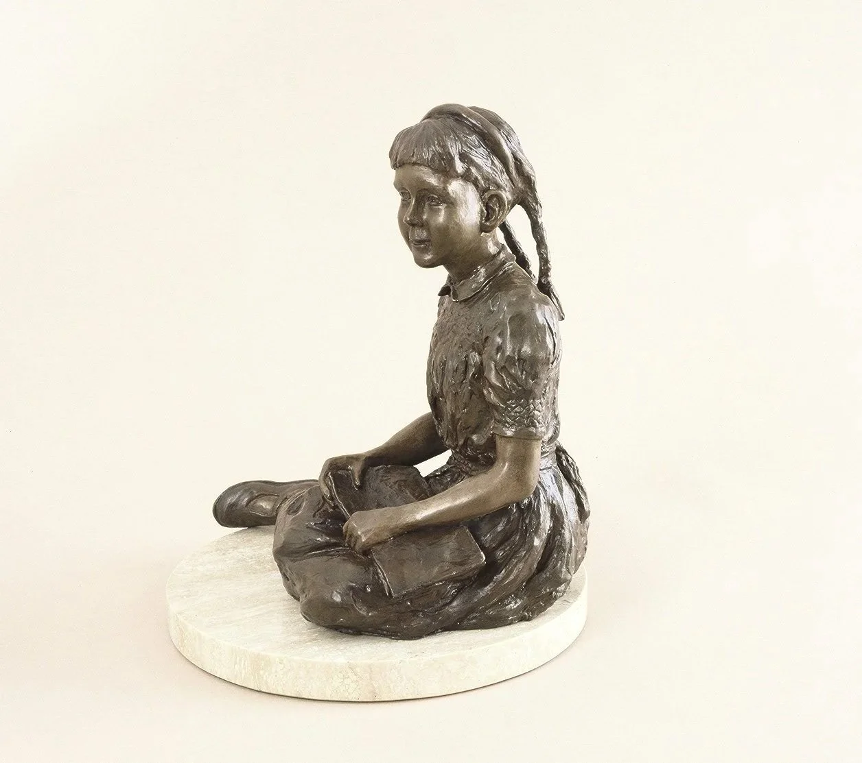 Girl with a Book Study small bronze sculpture of young girl sitting with legs to one side holding a book open on her lap wearing a short sleeved dress side view