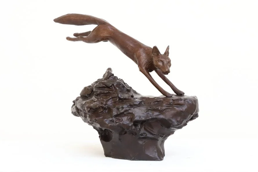 Fox study small bronze sculpture of fox leaping over rough ground with orange patina
