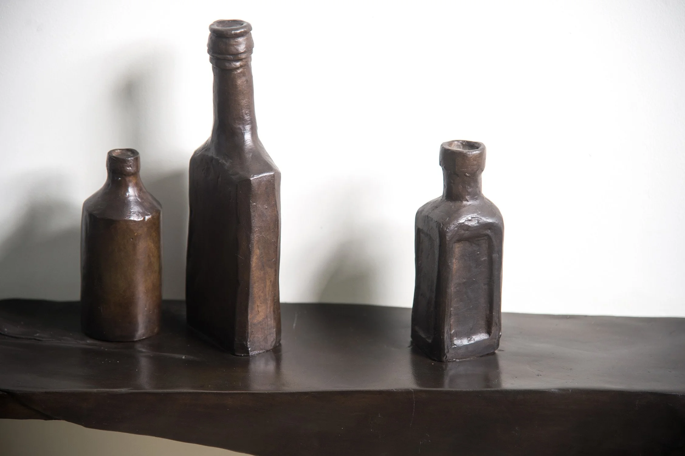 Still Life VIII life size bronze sculpture draped cloth and bottles on shelf close up view