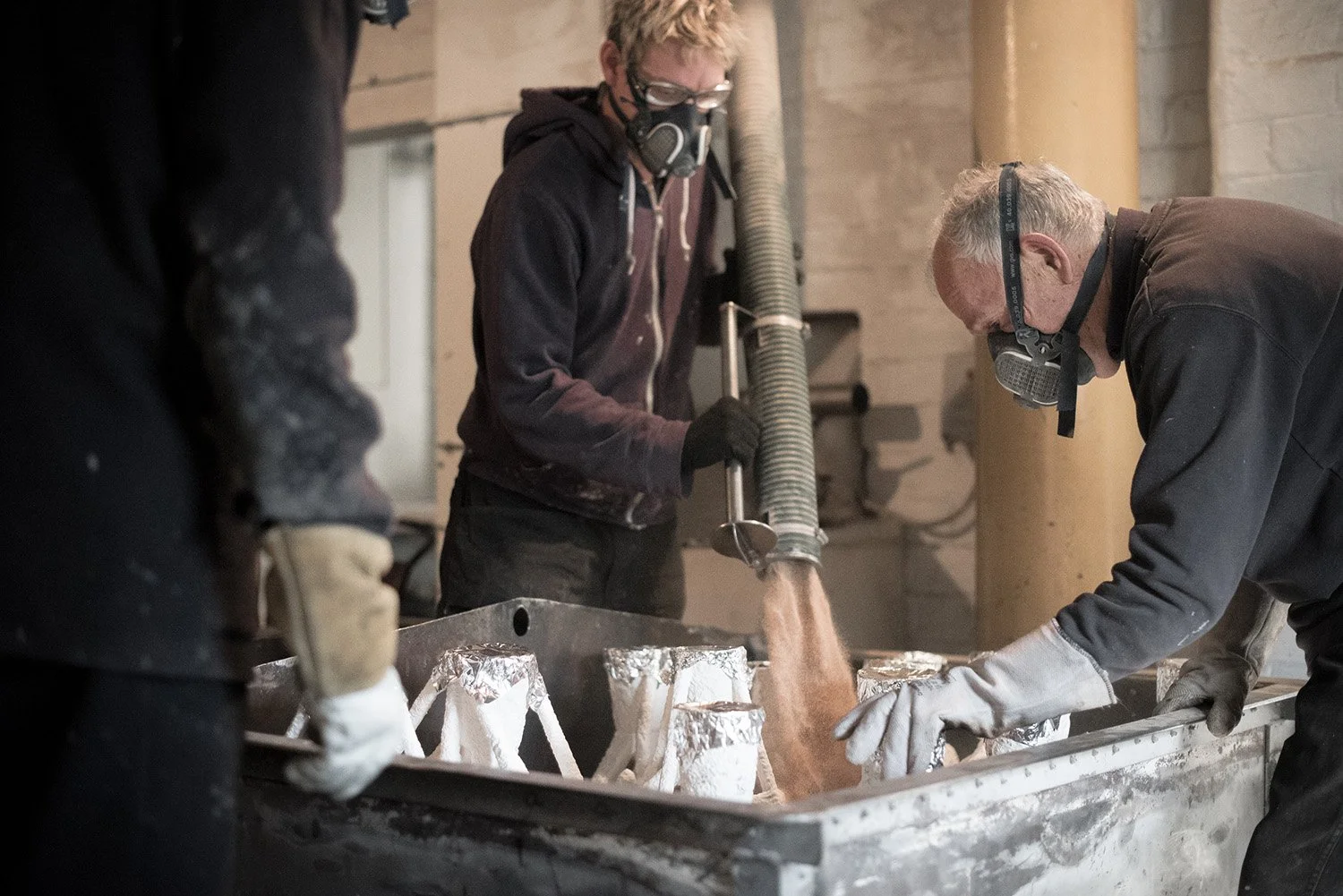 Foundry people secure moulds in sand for bronze pour wearing protective clothing 