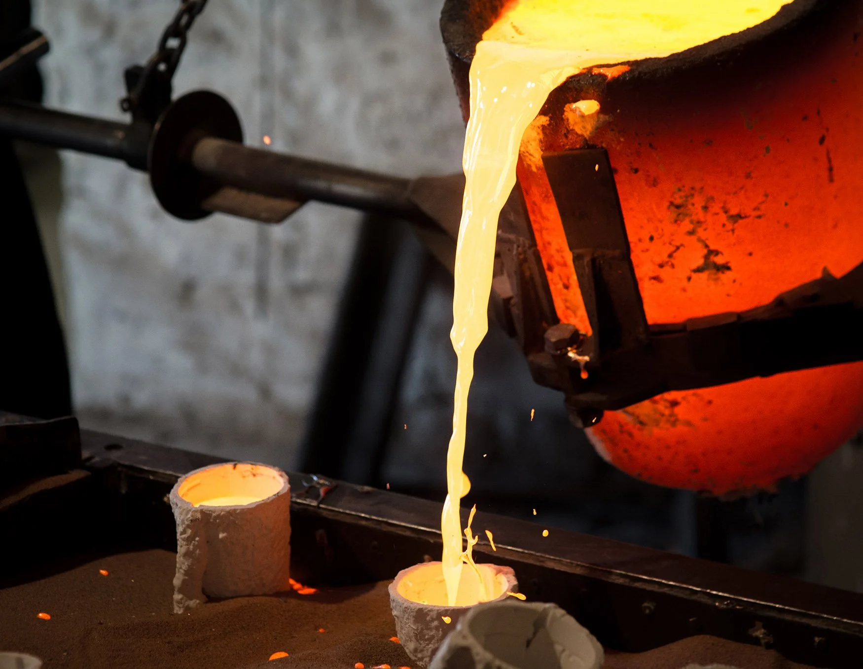 Red hot crucible tilts glowing molten bronze splashes into mould
