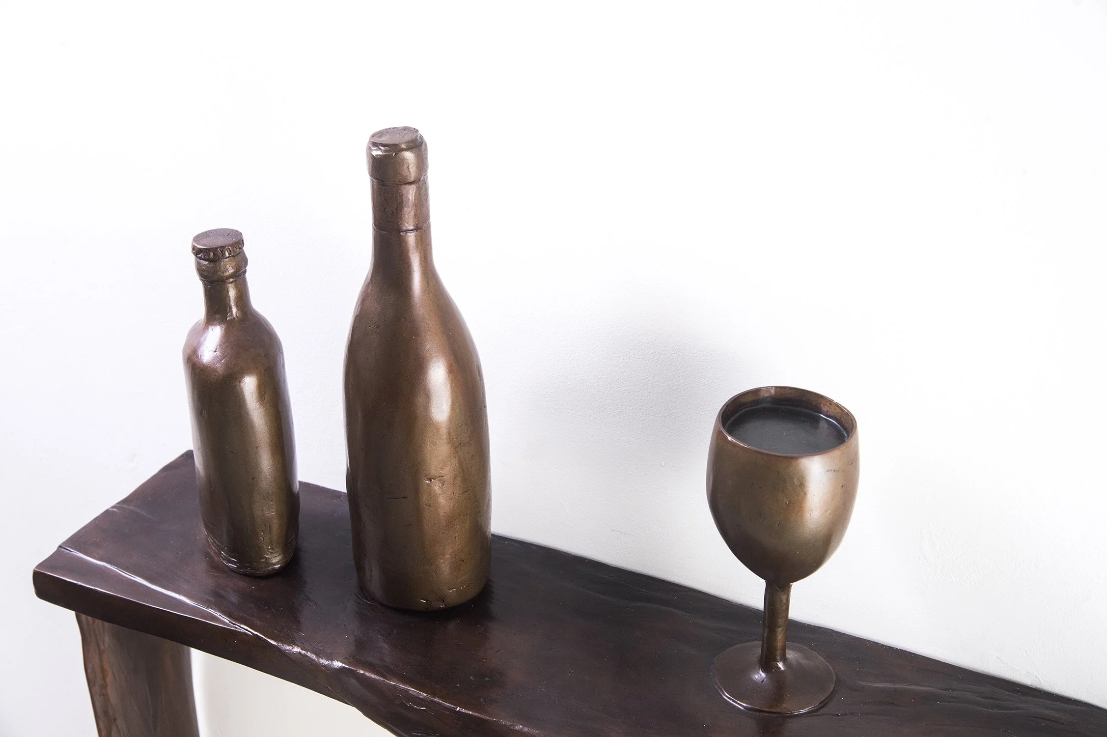 Still Life X life size bronze sculpture draped cloth bottles and full wine glass on shelf close up view