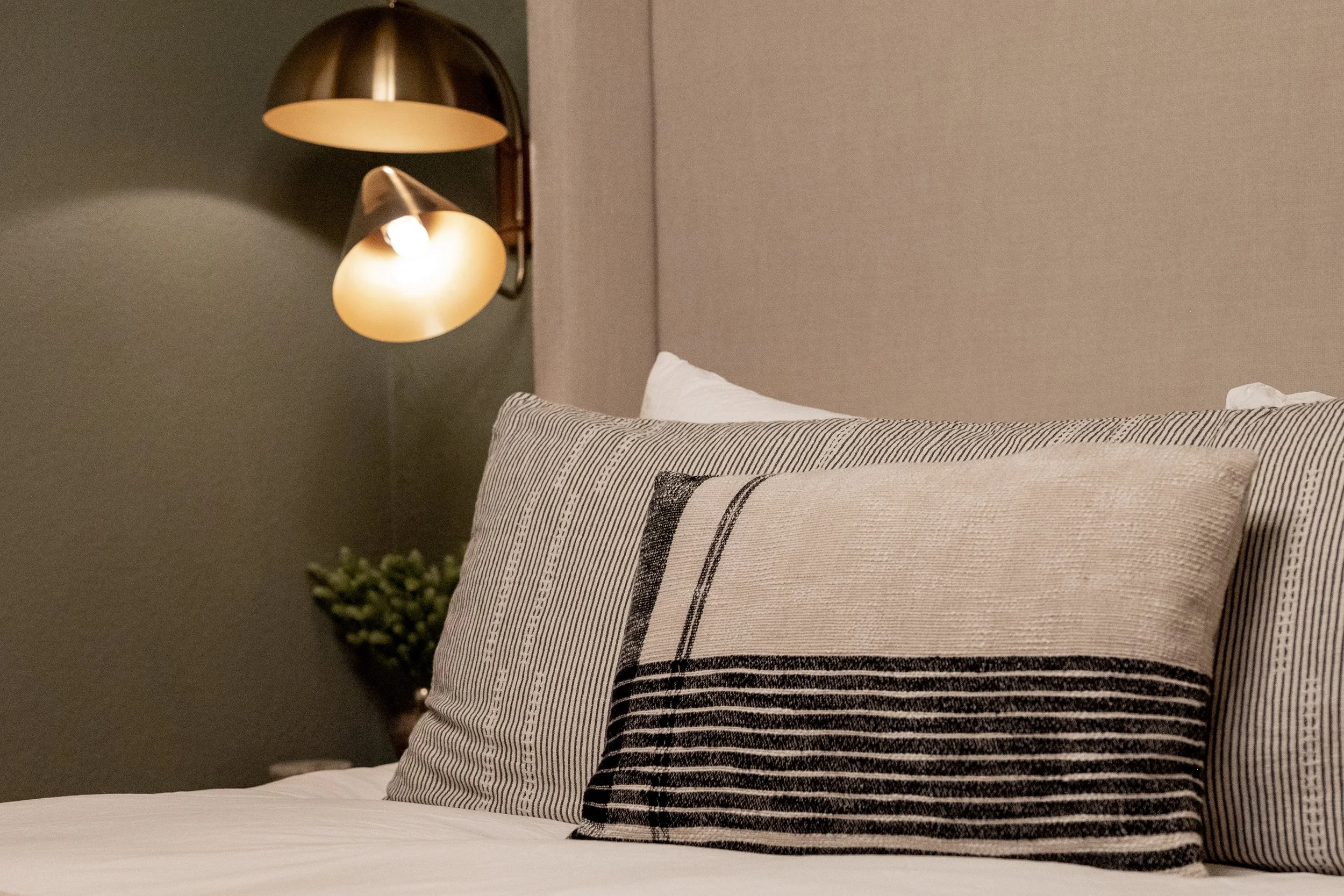 Cozy bedroom details with layered striped pillows, warm brass sconces, and soft ambient lighting - creating a calming, modern mountain retreat.