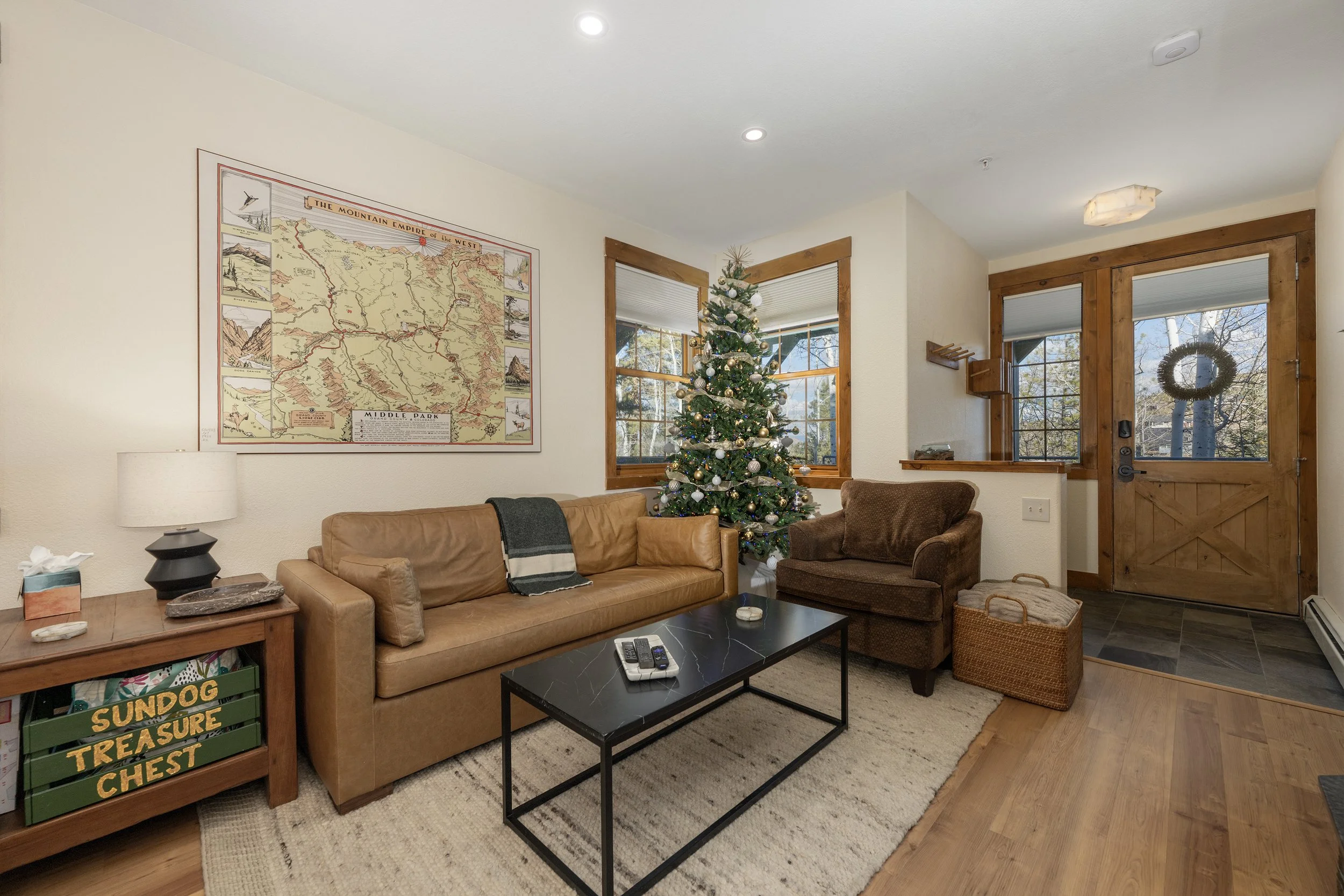 Inviting living room with leather sofa, cozy armchair, and holiday décor, featuring large windows and a historic map of the area.
