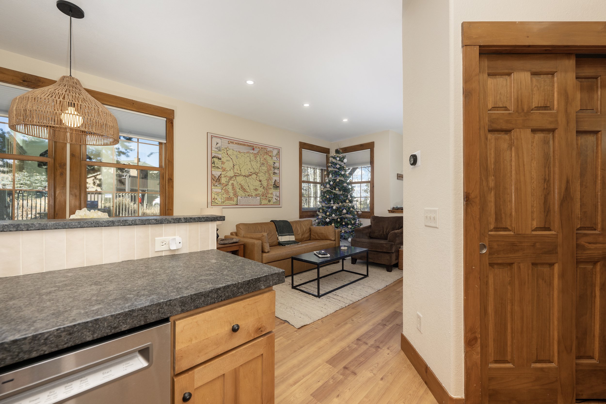 Bright, open layout with seamless flow from the kitchen into the living room. Cozy seating, warm wood accents, and big windows create an inviting space - complete with a seasonal tree for festive stays.
