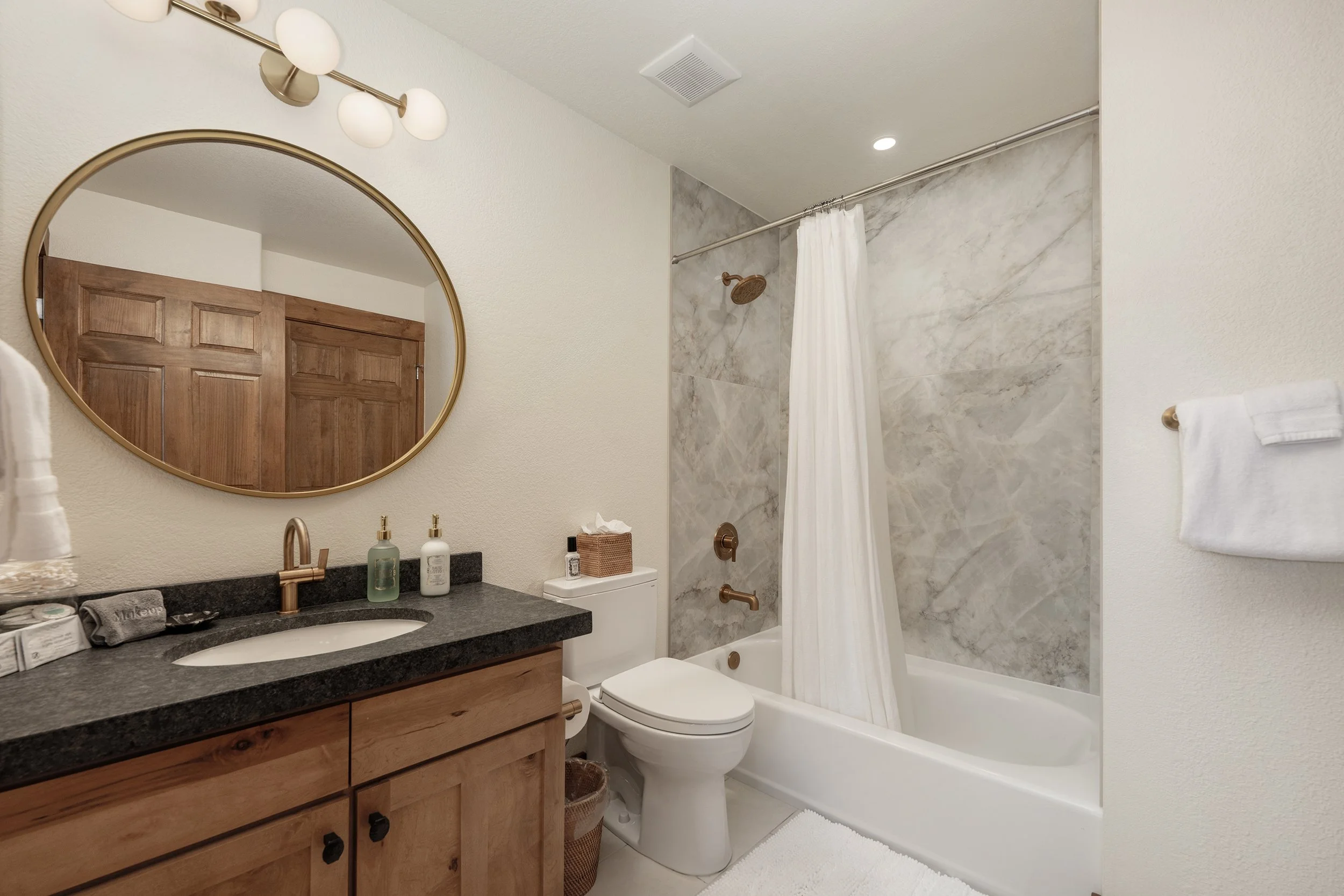 Freshly remodeled bathroom with marble-look tile, gold fixtures, plush towels, and hotel-quality toiletries.