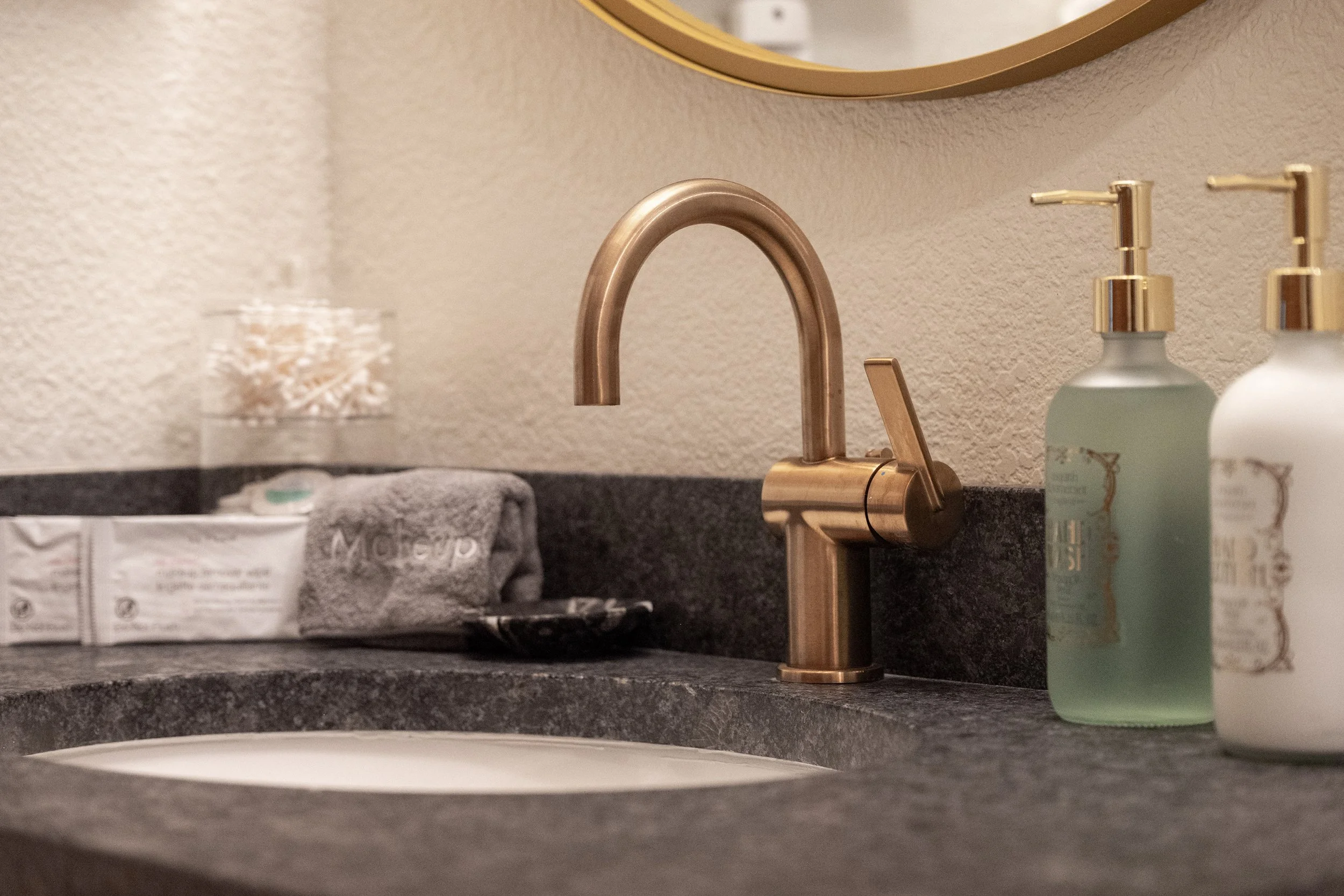 Elegant bathroom details featuring a brushed-brass faucet, makeup towels, cotton swabs, and hand soaps - everything arranged for a comfortable, hotel-level stay.