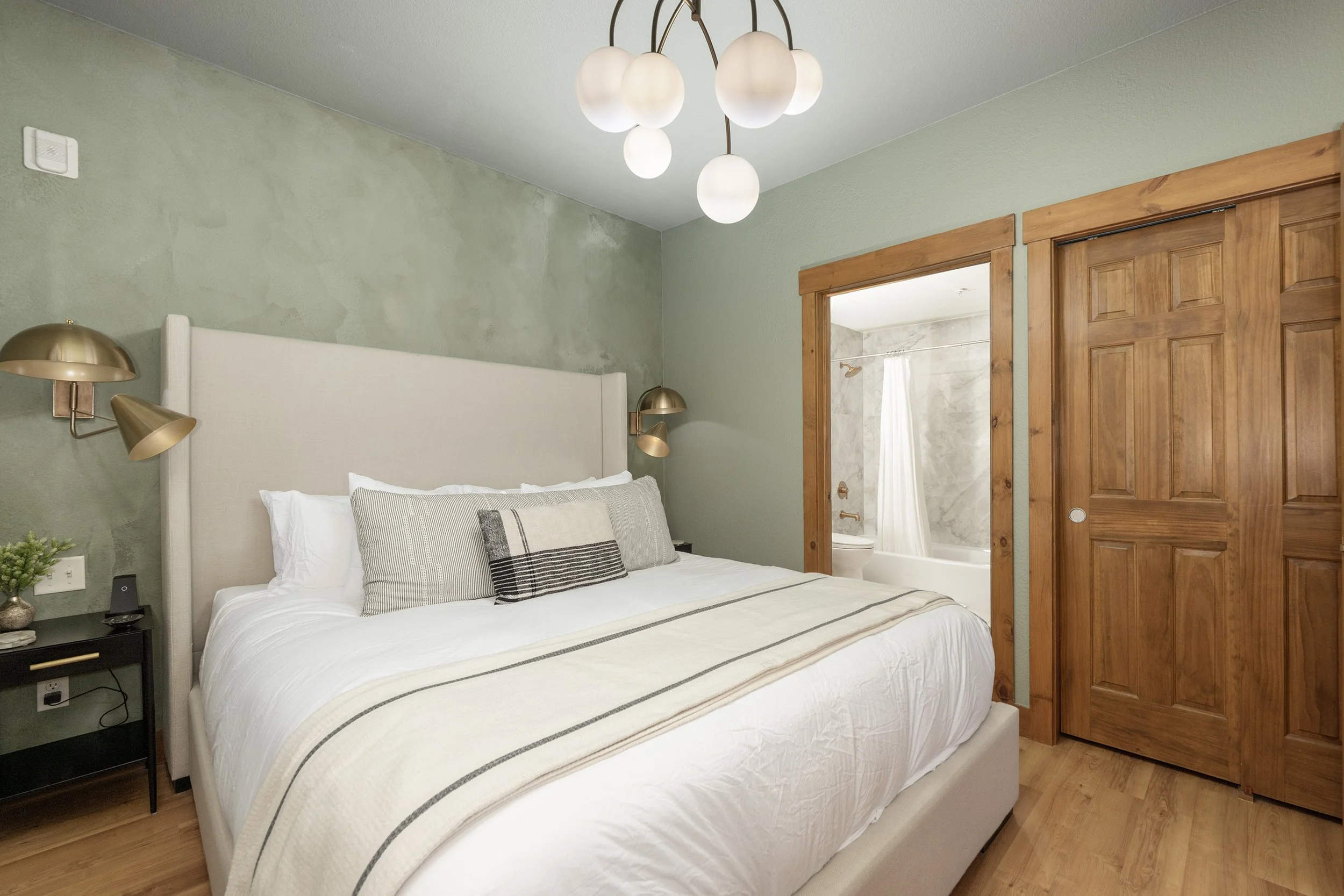 Relax in the serene primary bedroom featuring a king bed with Brooklinen linens, soft green walls, and ensuite access to the updated bathroom.