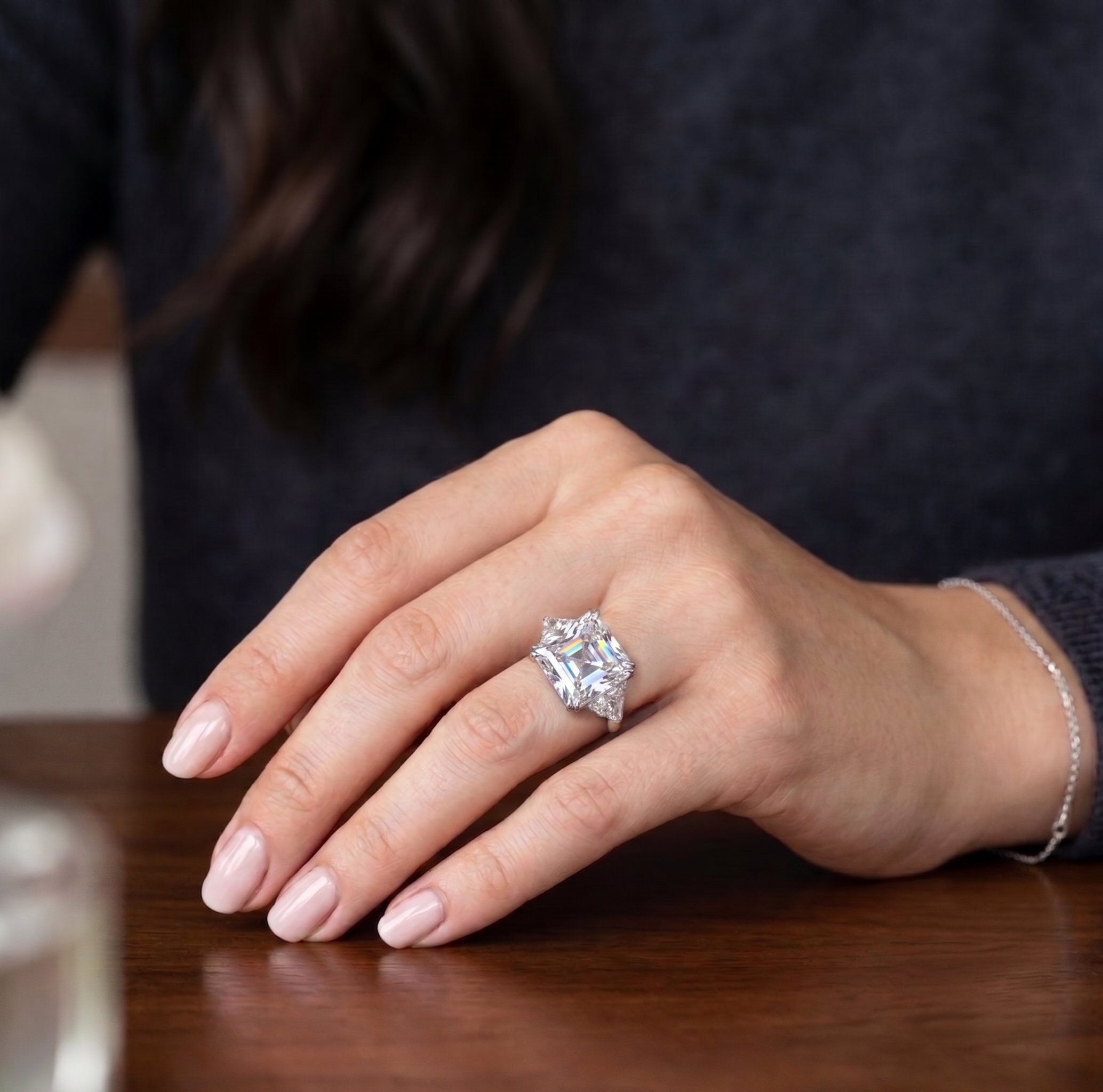 Hände mit einem großen Diamantring auf einem dunklen Holztisch, Nahaufnahme.