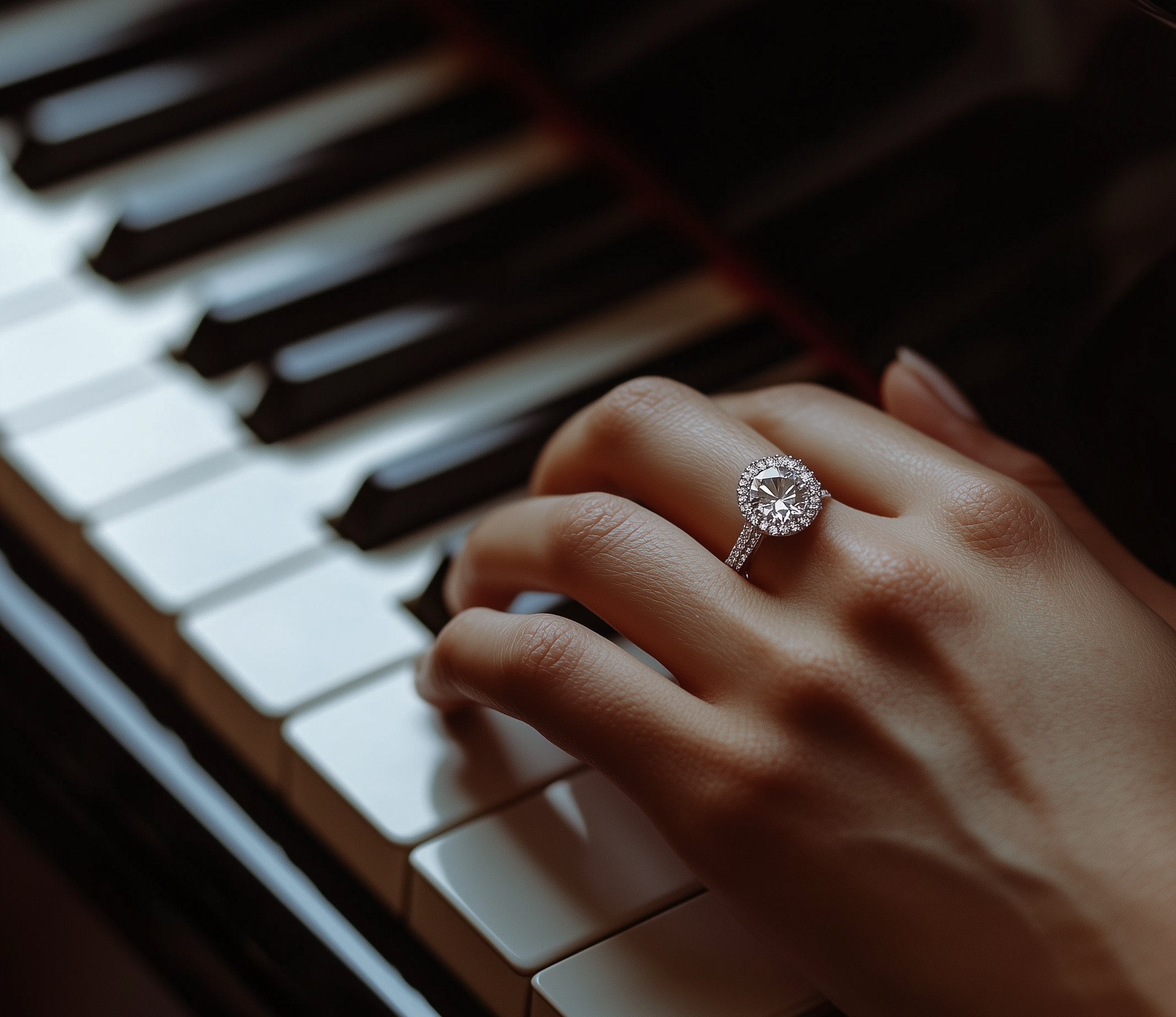 Nahaufnahme einer Hand mit einem Verlobungsring, der einen großen, runden Diamanten und einen Diamantschmuck umkreist, während sie eine Klaviertastatur berührt.