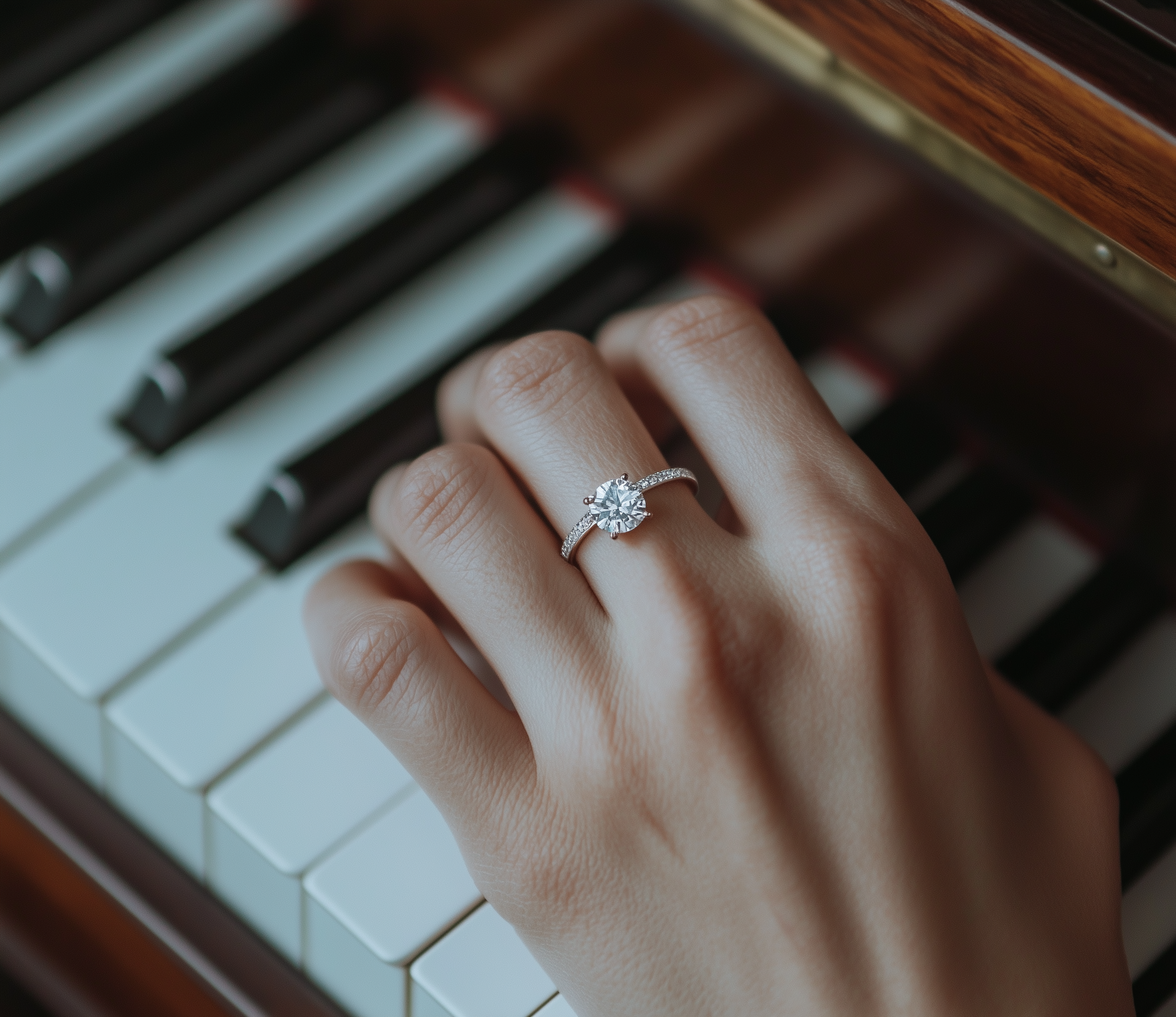 Ein Handmodell trägt einen Verlobungsring mit einem großen Diamanten und kleinen Diamanten an einem Frauenring. Im Hintergrund sind Klaviersaiten sichtbar.