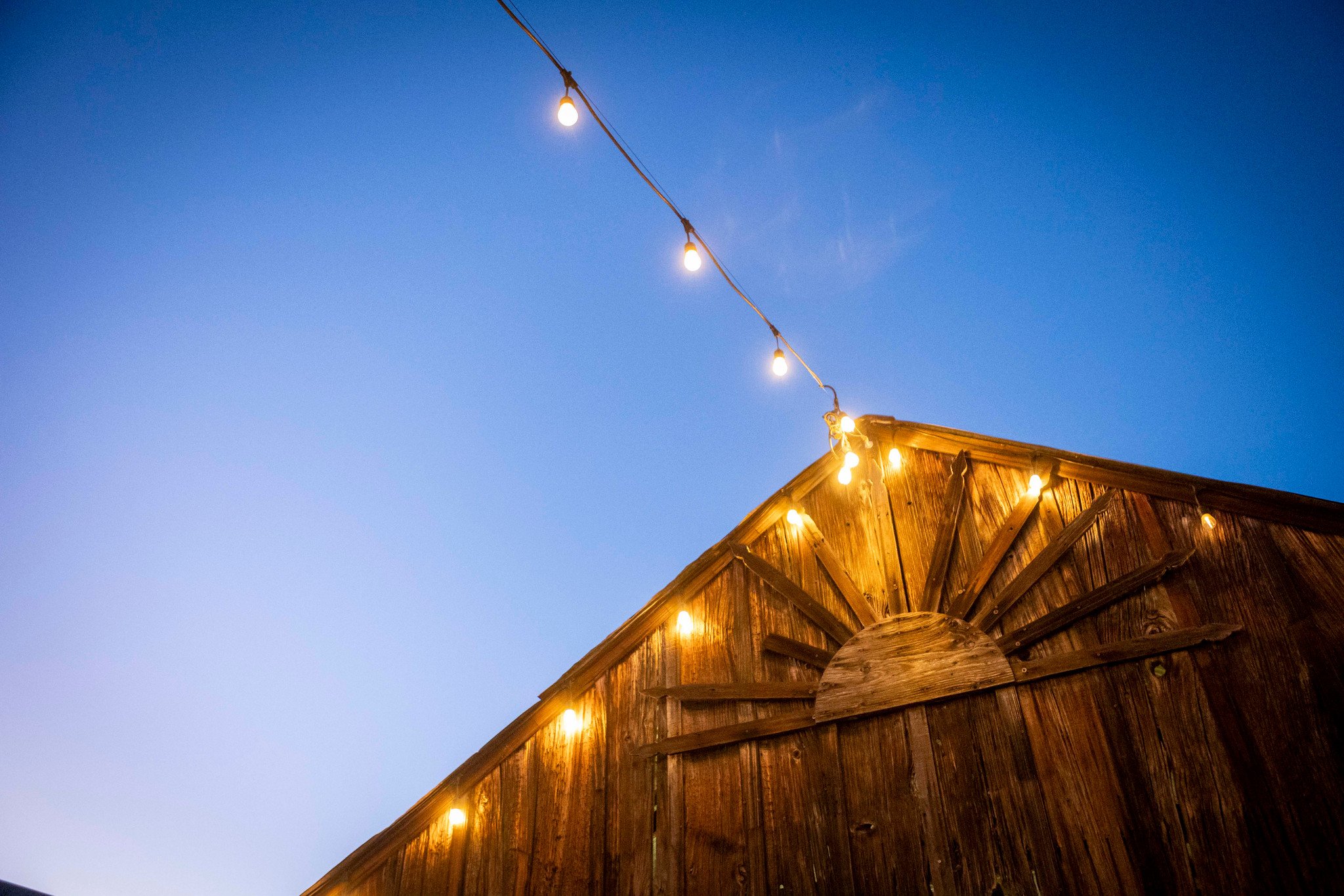 Wooden barn with string lights hanging on it under a blue evening sky.