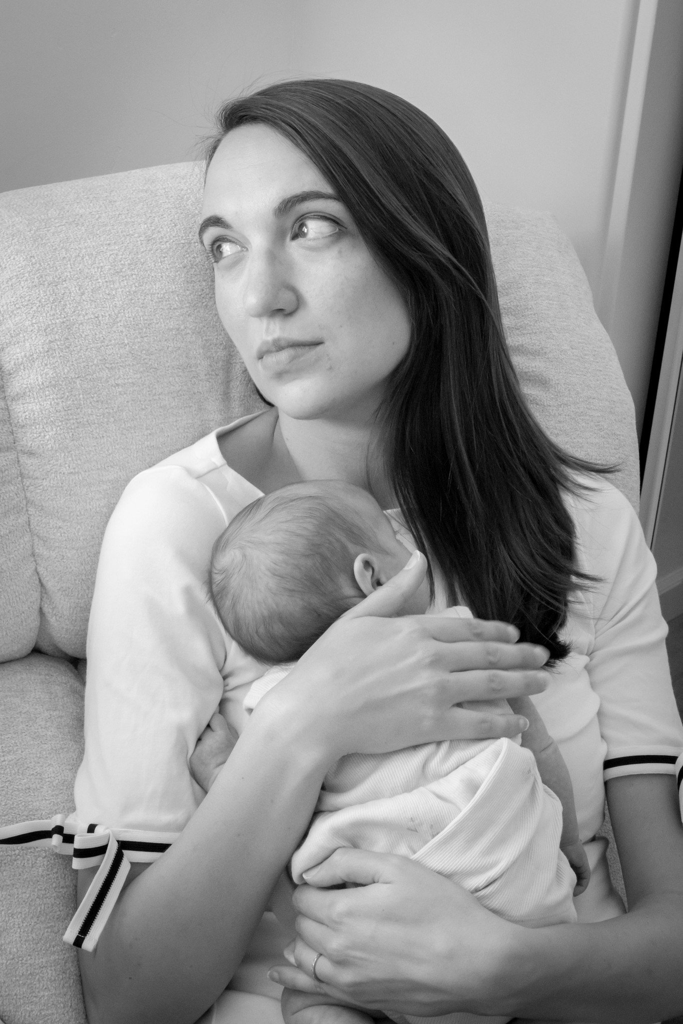 A woman with long dark hair holding a baby while sitting on a couch, in black and white.