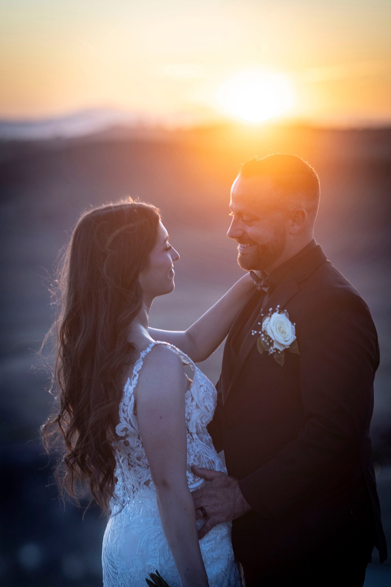 A bride and groom smiling at each other during sunset on a beach.