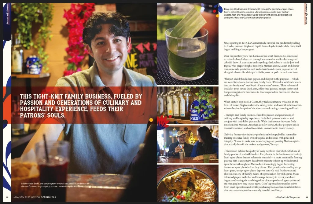 A man with dark, curly hair smiling in a colorful, lively bar or restaurant setting. The image is part of a magazine spread with text about a family-owned business.