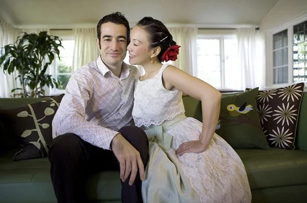 A man and woman sitting on a green couch in a bright living room, smiling and close to each other.