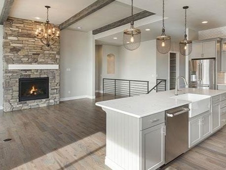 Open-concept living room and kitchen with stone fireplace, chandelier, modern pendant lights, and white kitchen island.