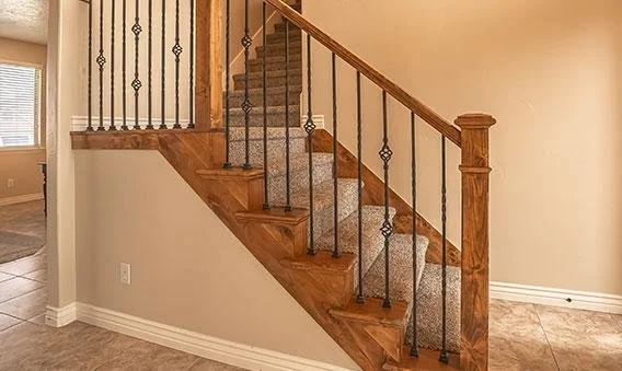 Wood staircase with black metal railing and beige carpeted steps inside a home.