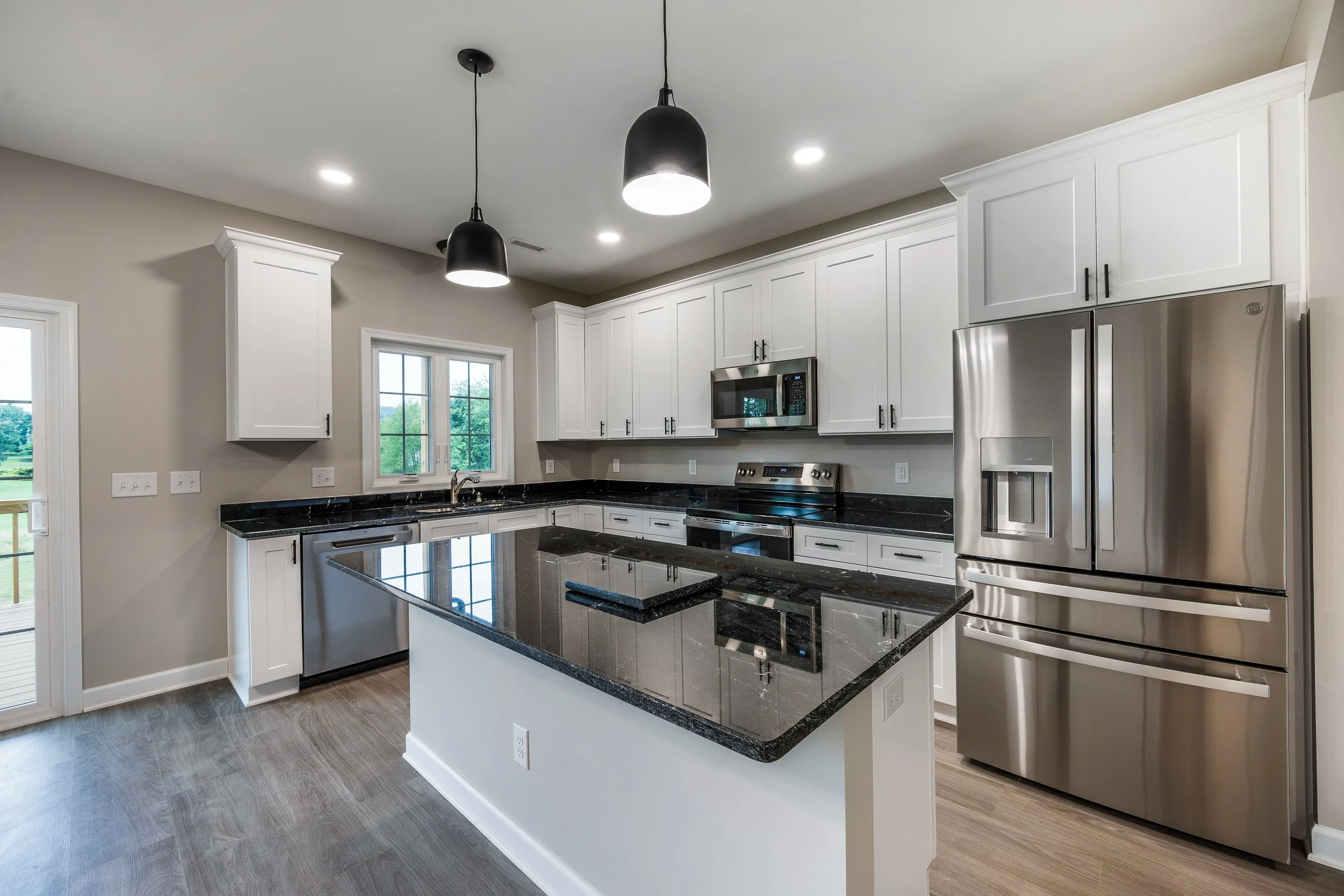 Modern kitchen with white cabinetry, black granite countertops, stainless steel appliances, a kitchen island, and pendant lights.