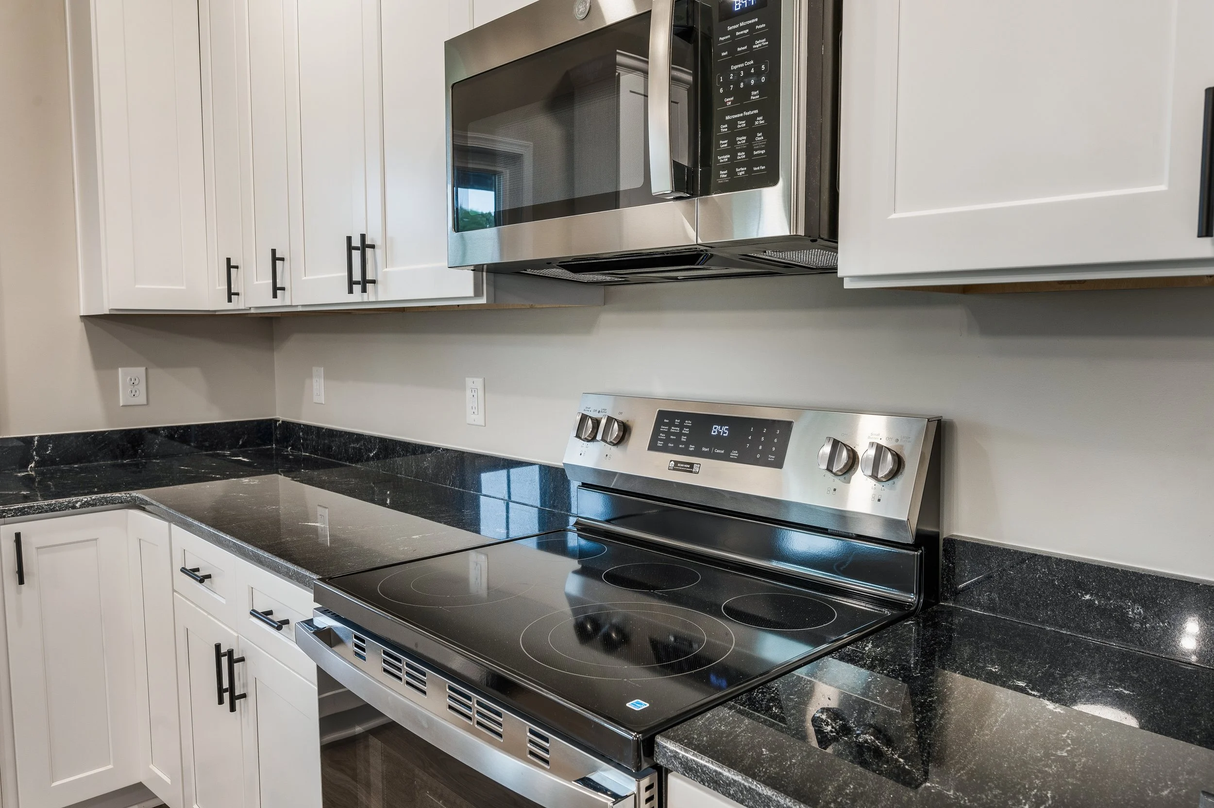 Kitchen with white cabinets, black granite countertops, stainless steel microwave, and electric stove.