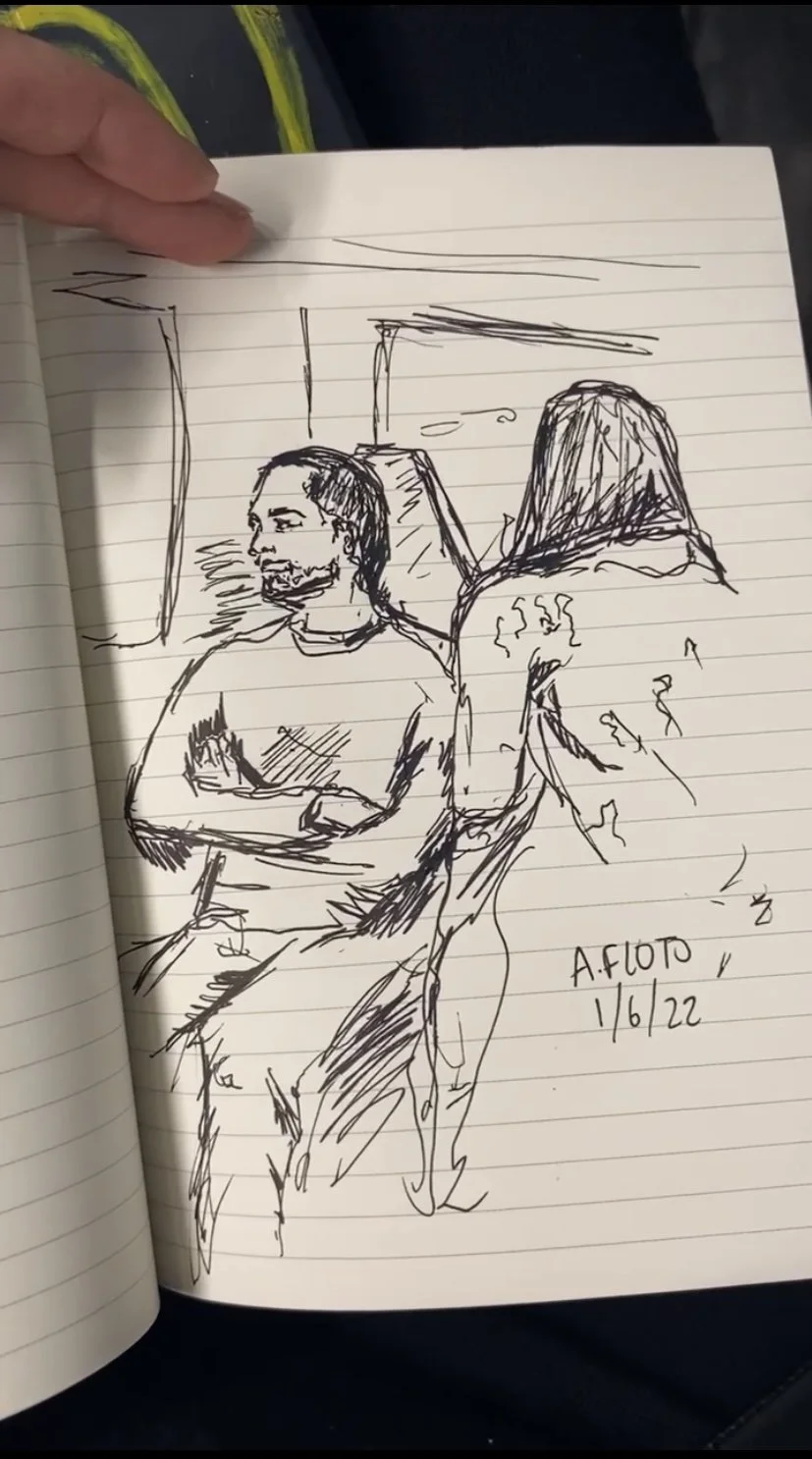 A hand-drawn sketch in a notebook showing two people seated on a train, one facing forward and the other facing sideways. The sketch is signed "A. Floto 1/6/22."