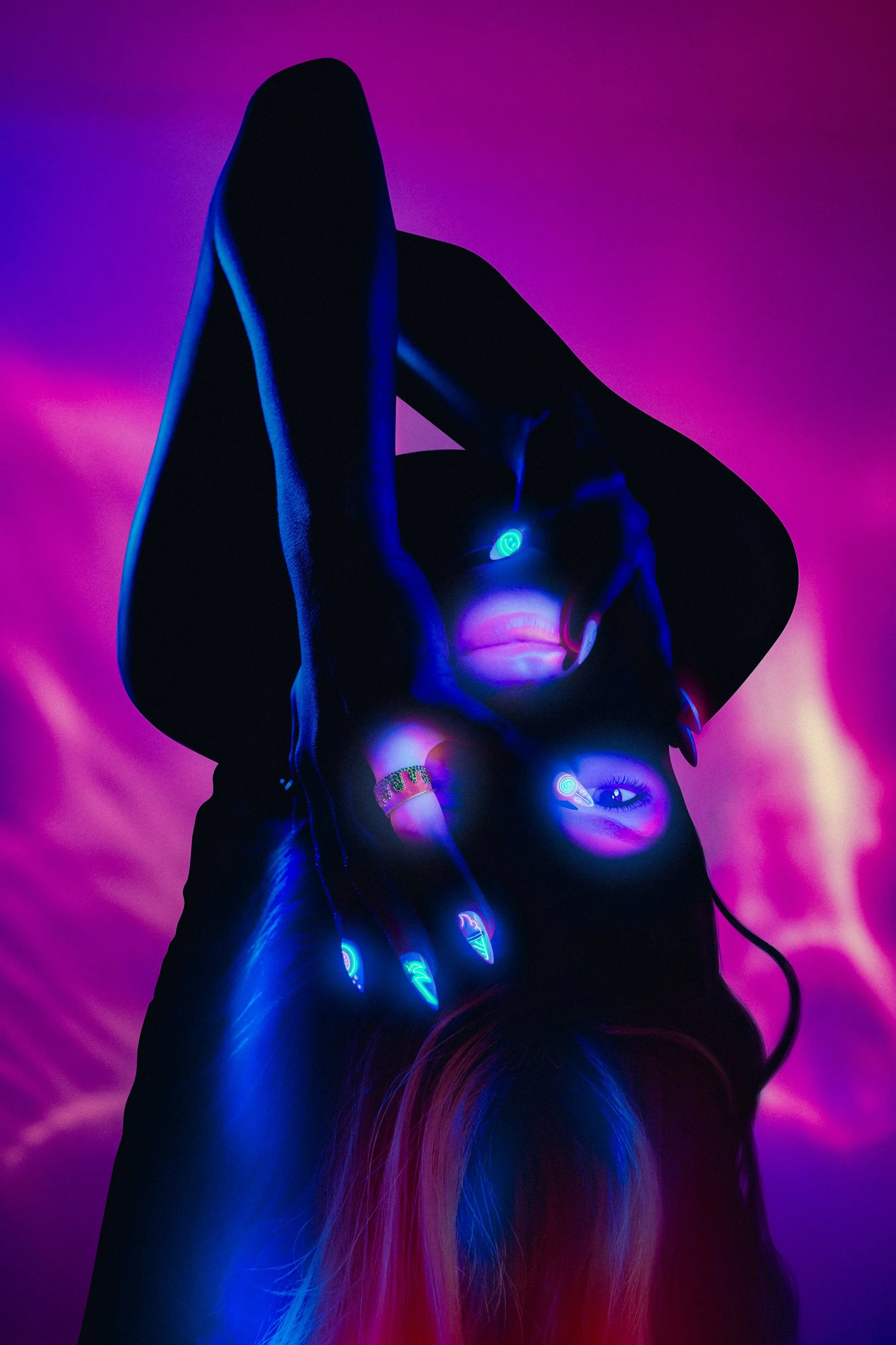 A person with glowing neon nails and face paint in blue and pink lighting.