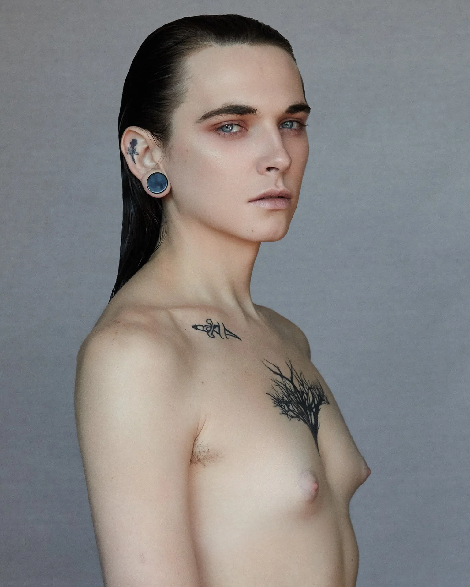 Androgynous person with tattoos and stretched earlobes.
