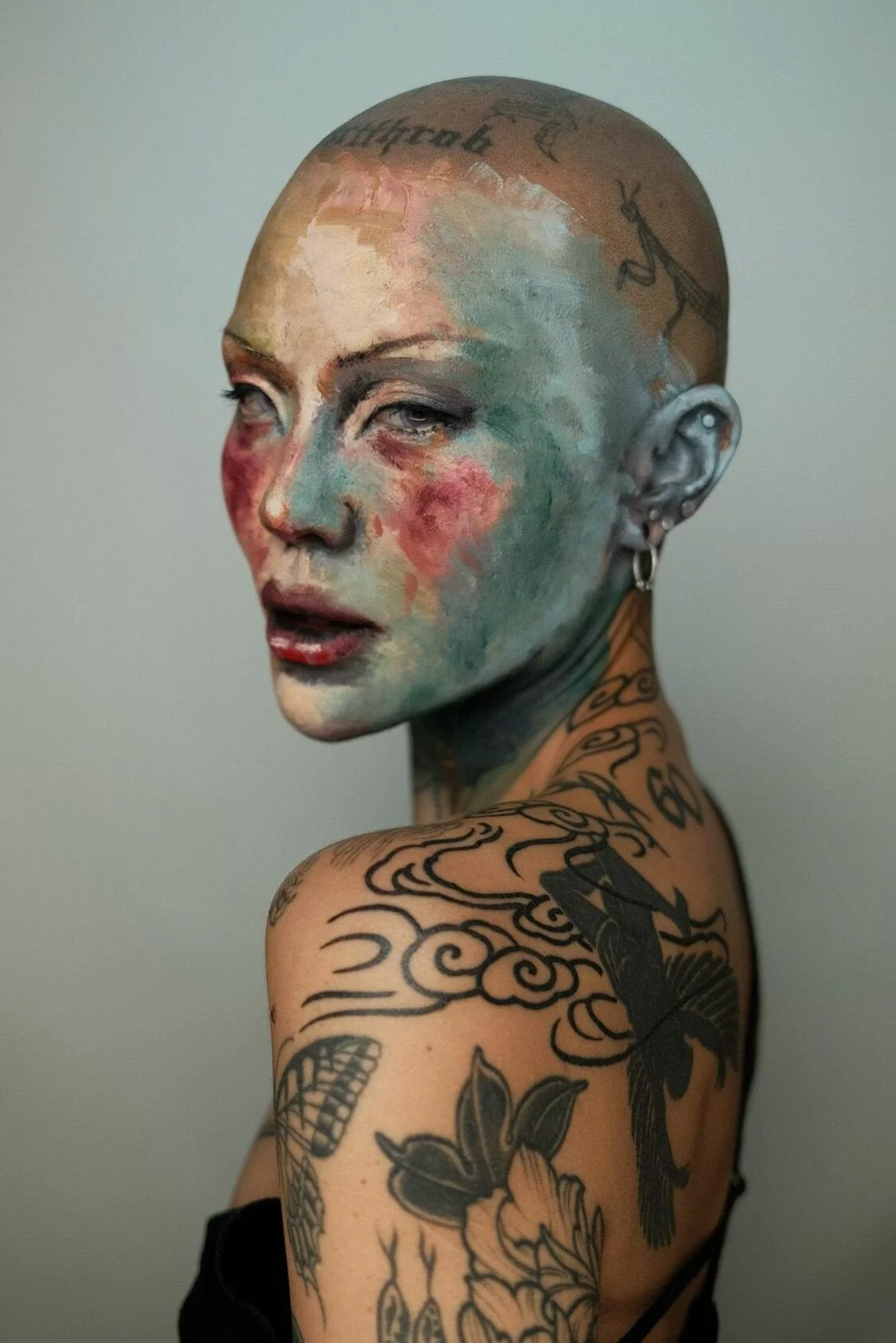 Person with colorful painted face and tattoos on head and shoulder