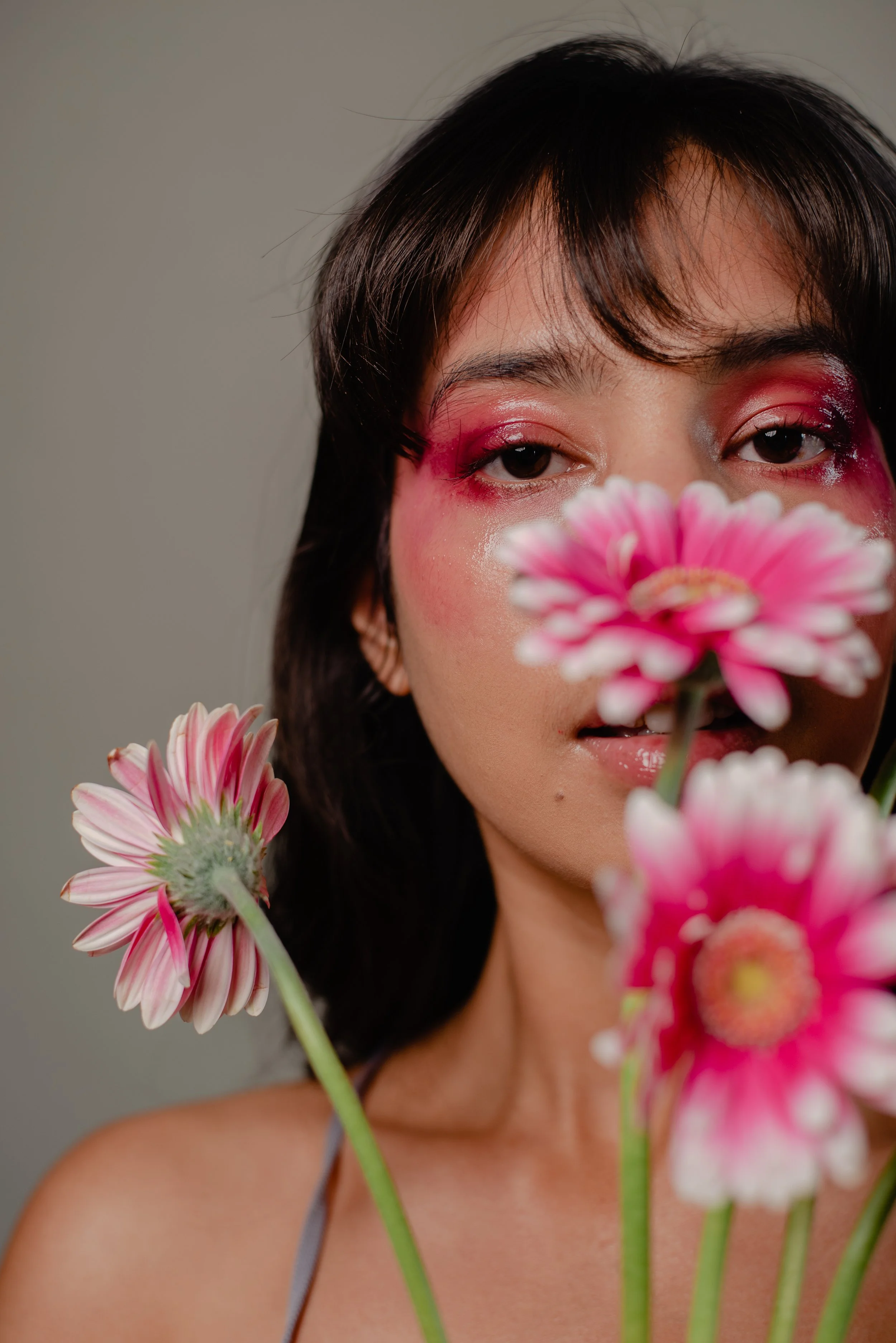 Person with pink eye makeup partially obscured by pink gerbera daisies
