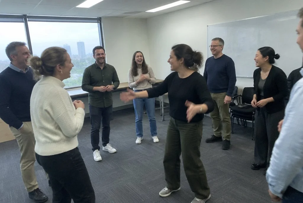 Office team standing in a circle and laughing during an improv team building workshop at their workplace