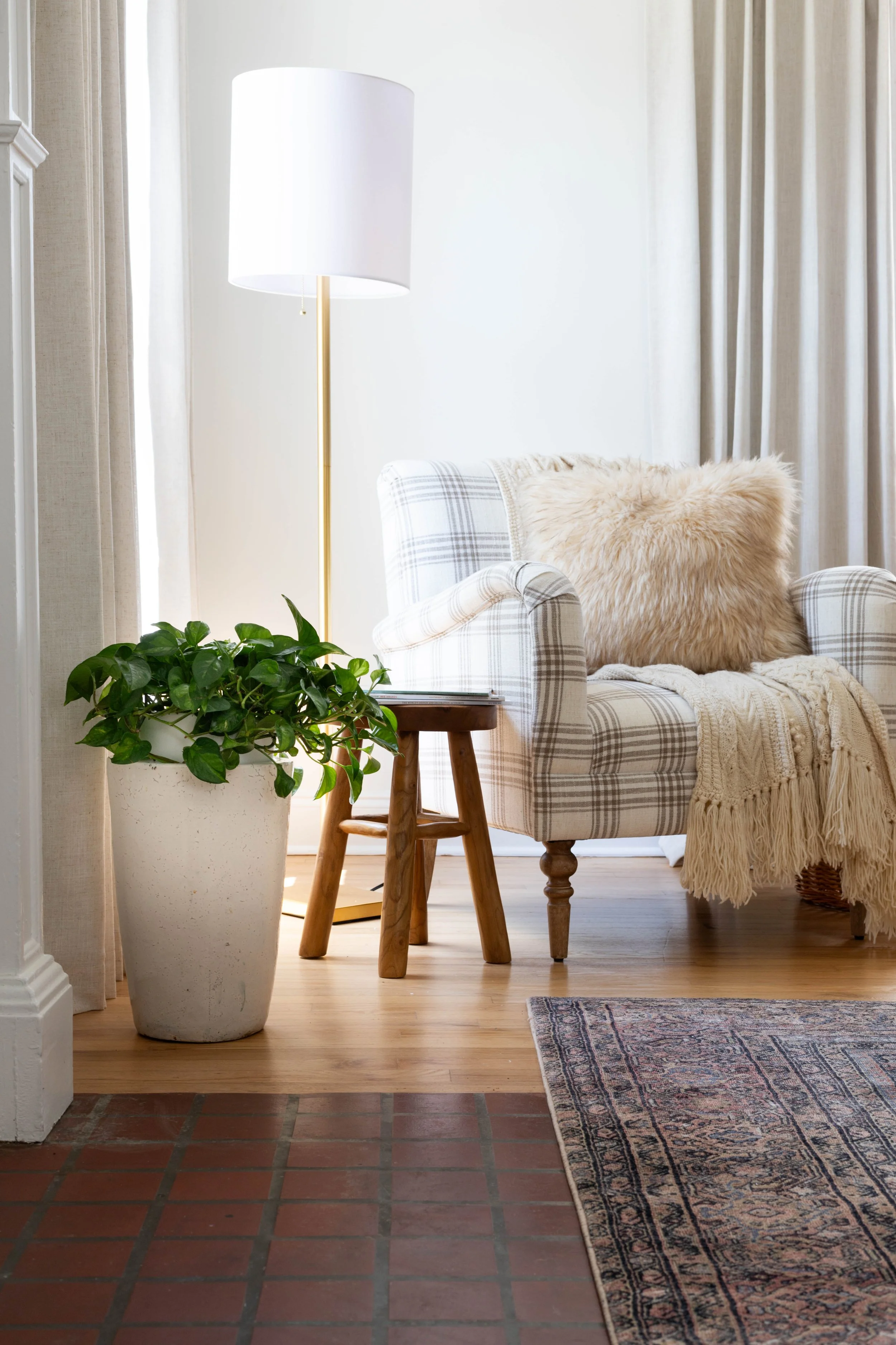 a small wooden stool flanking an plaid accent chair and floor lamp