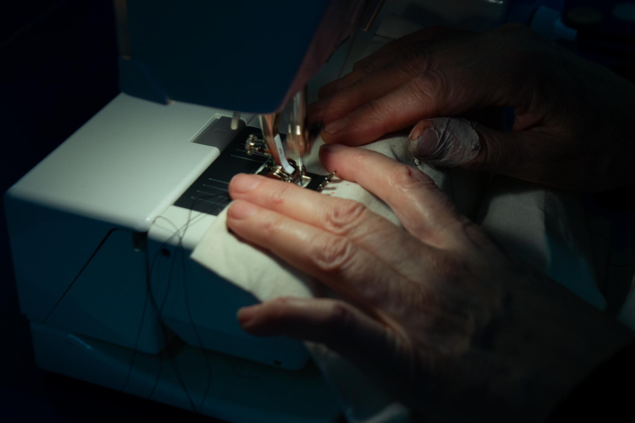 Close-up of hands sewing fabric with a sewing machine in a dimly lit room.