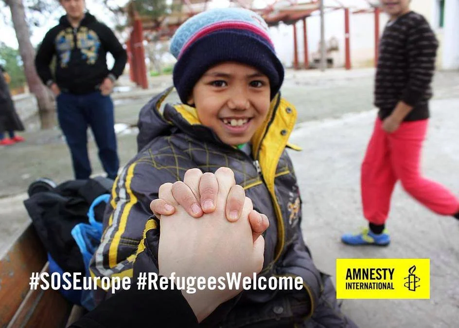 A smiling boy in a winter jacket and a beanie shaking hands with someone outdoors, with two other children in the background. The image includes hashtags #SOSEurope and #RefugeesWelcome, and the Amnesty International logo.