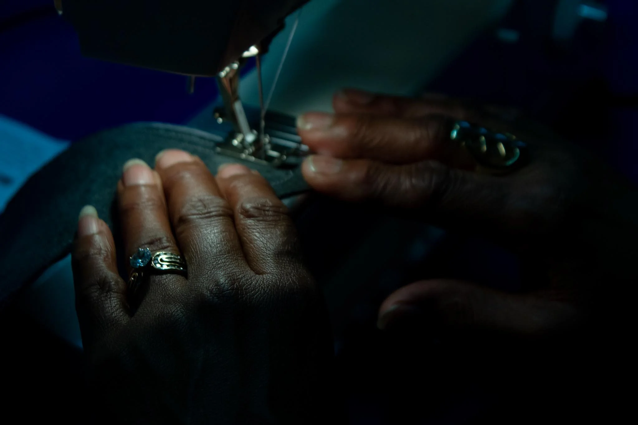 A person operating a sewing machine with their hands guiding fabric, wearing rings on fingers.