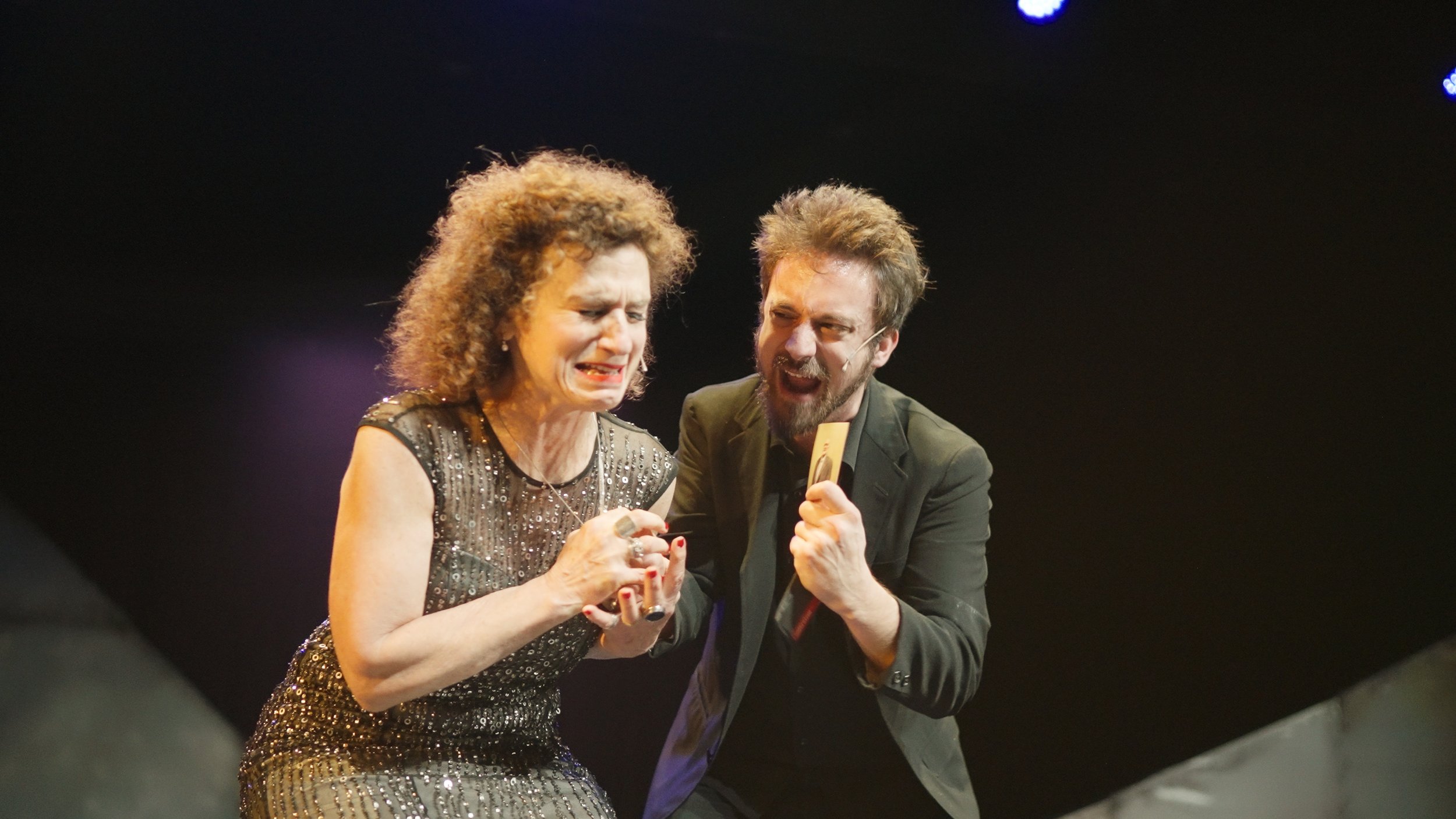 Woman and man performing on stage, emotional moment, woman appears upset, man is speaking into microphone.