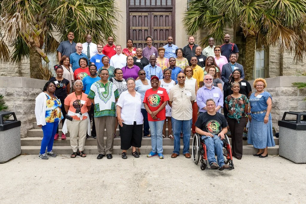 Group of people posing for a photo outside a building with palm trees