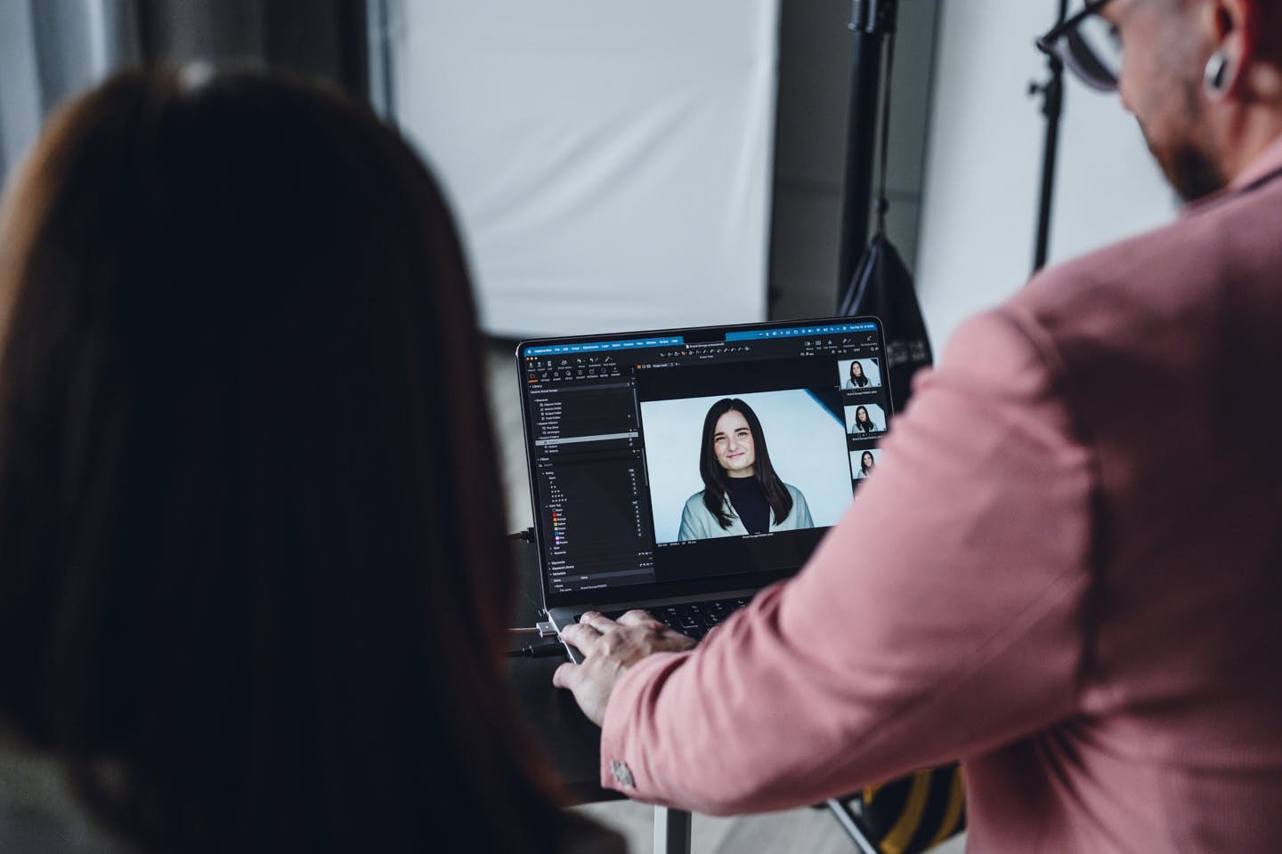 Photographers working on a portrait photo shoot with a woman on a computer screen, in a studio with professional lighting equipment.
