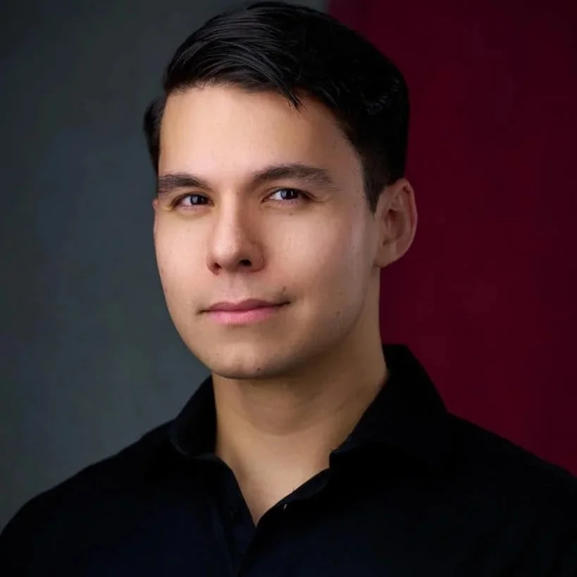 Portrait of a young man with dark hair, wearing a black shirt, against a background split between dark gray and deep red.